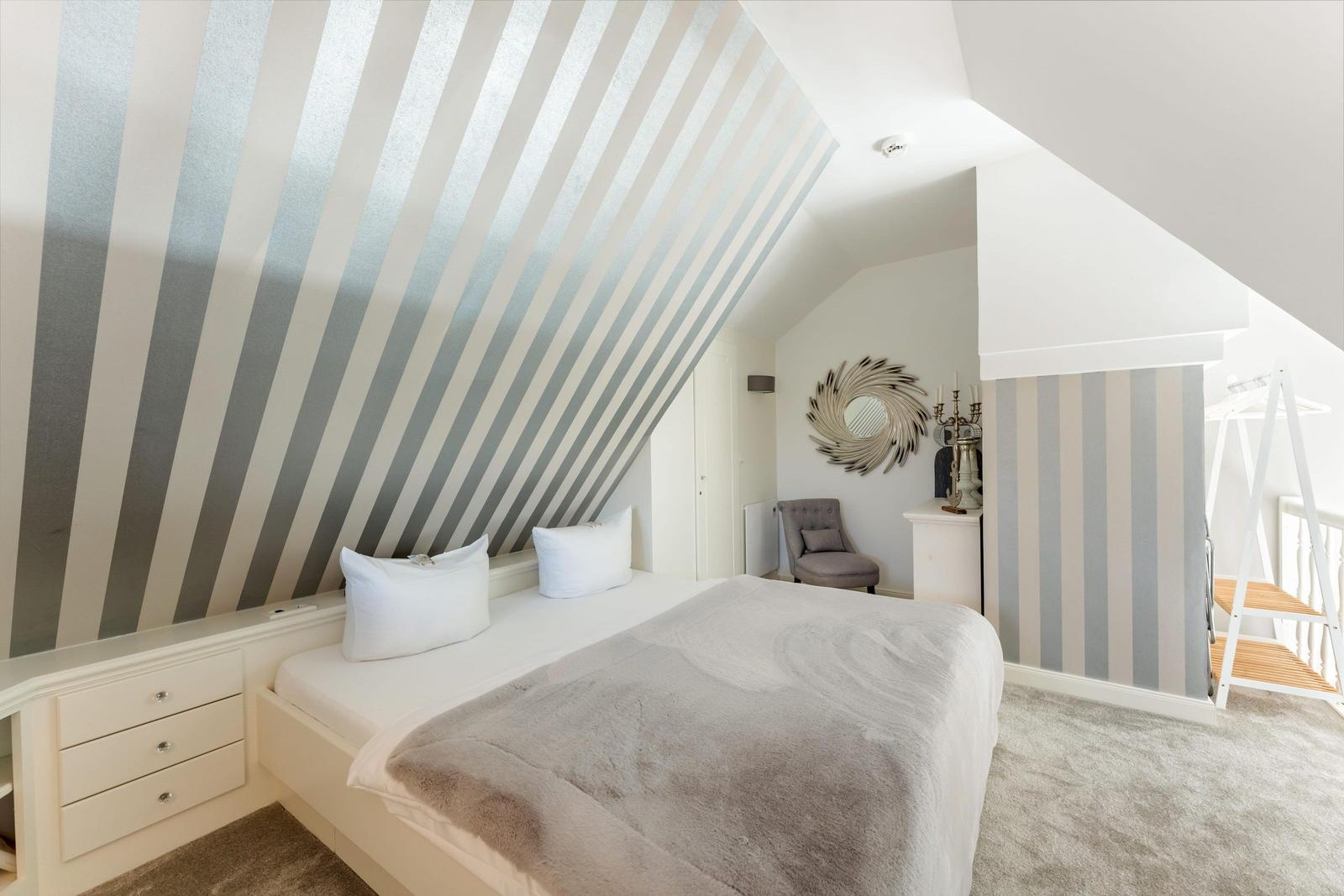 Bedroom with sloped ceiling, striped wall, and white bed.