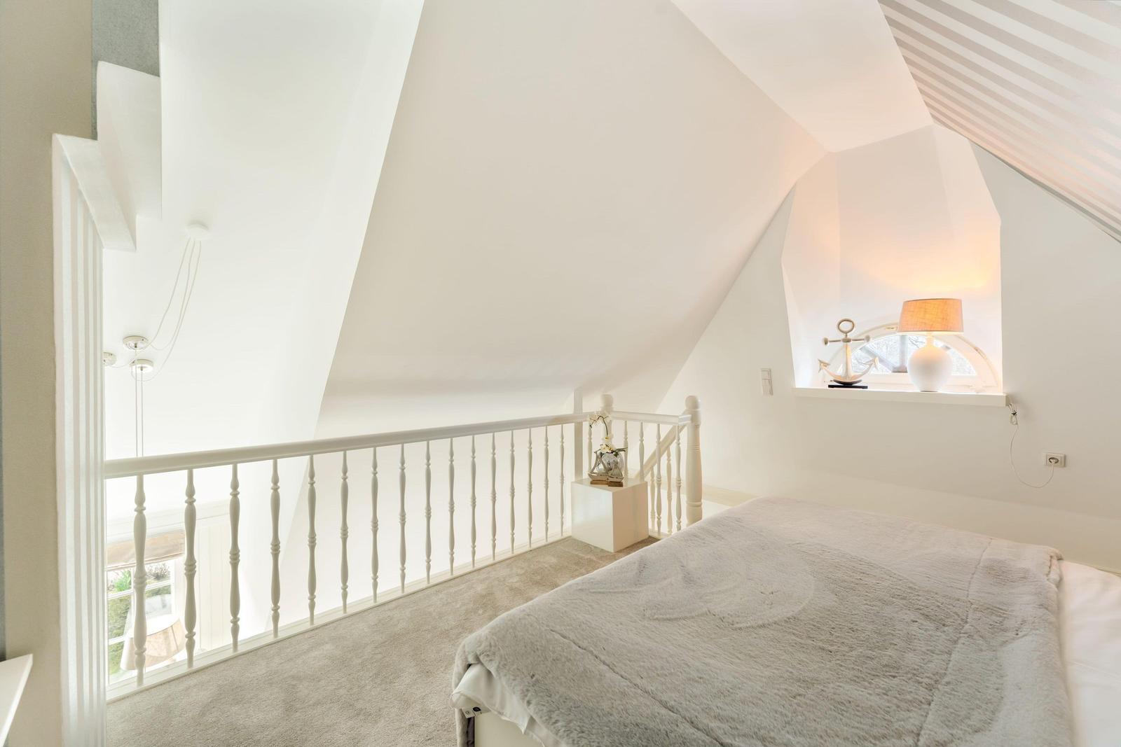 Bedroom with sloped ceiling, bed, window, and white balustrade.