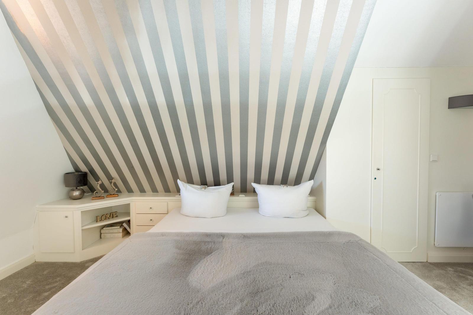 Bedroom with striped wall, white bed, and nightstand.