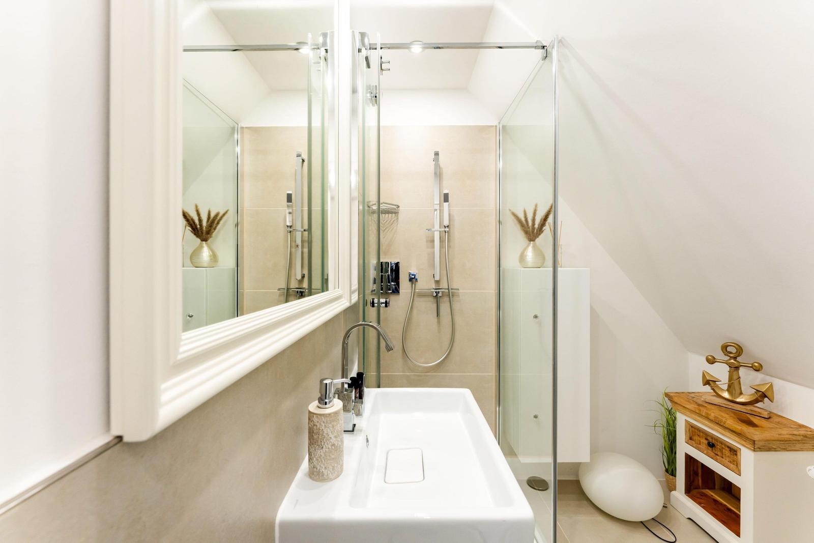 Bathroom with shower, sink, and mirror. Wooden cabinet with anchor decoration.