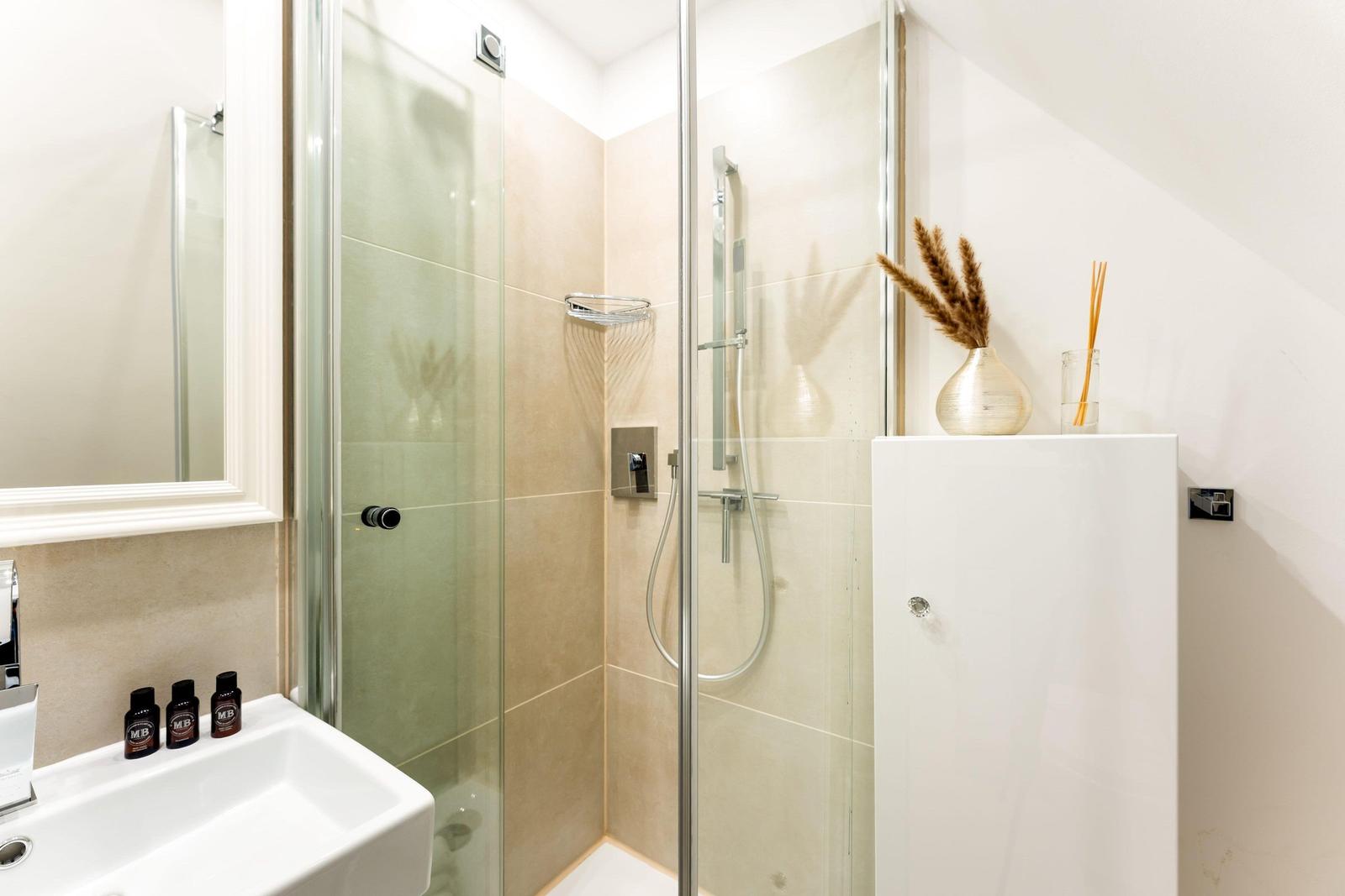 Bathroom with shower, sink, and mirror. Decorative vase and soap.