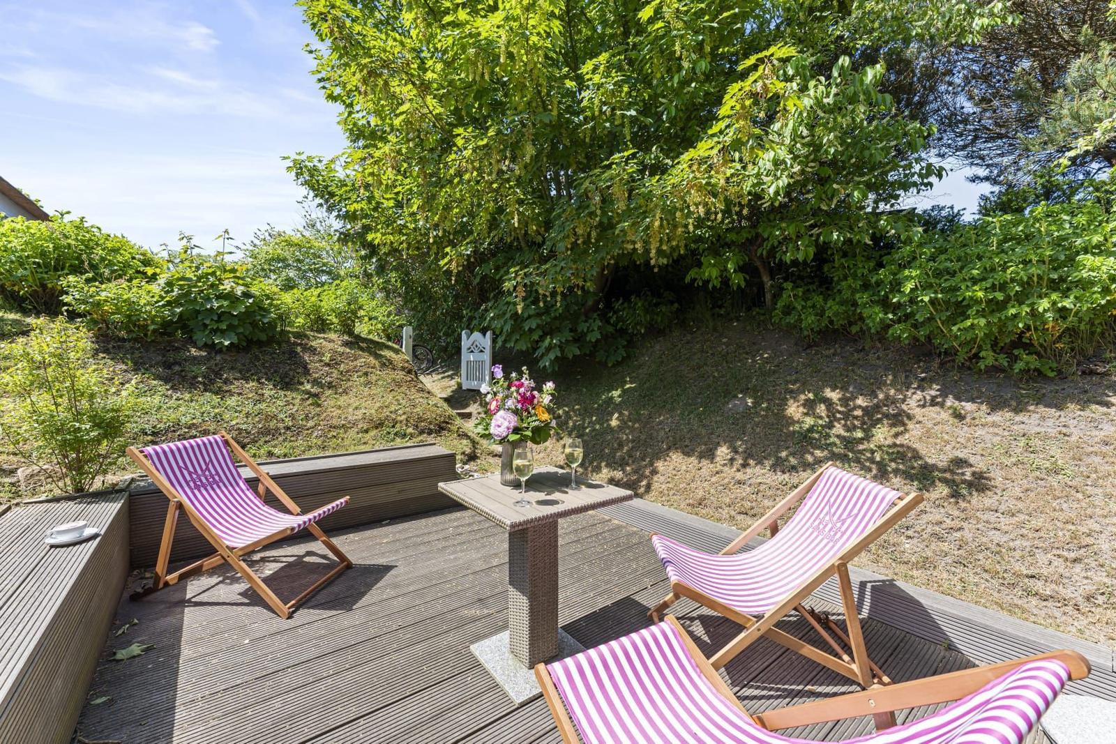 Terrace with three deck chairs and table under trees.