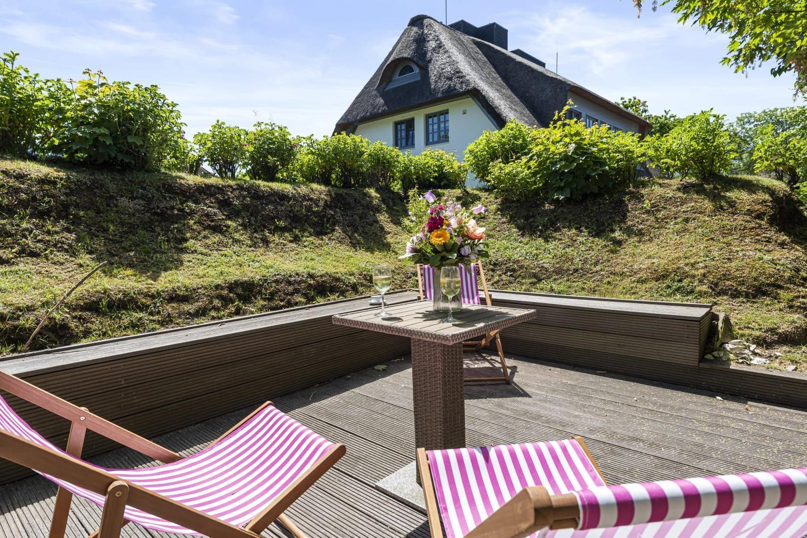 Terrace with loungers and table. House with thatched roof in background.
