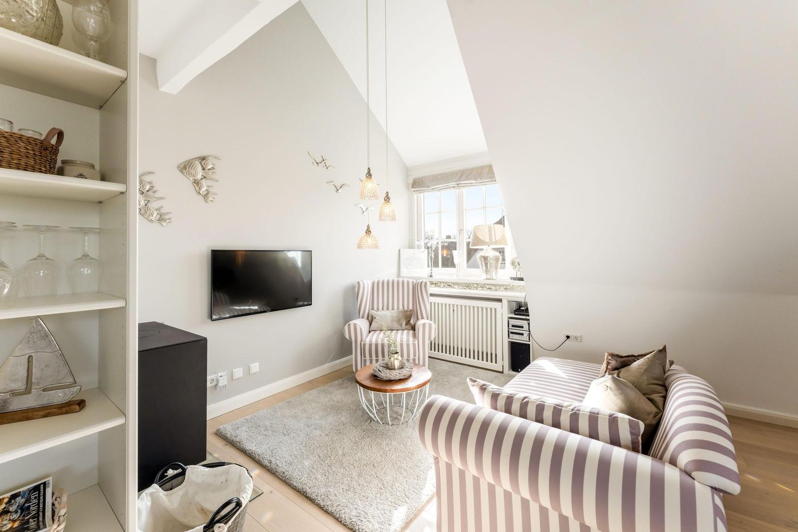 Living room with sofa, armchair, TV, and window. Shelf with glasses and decor.