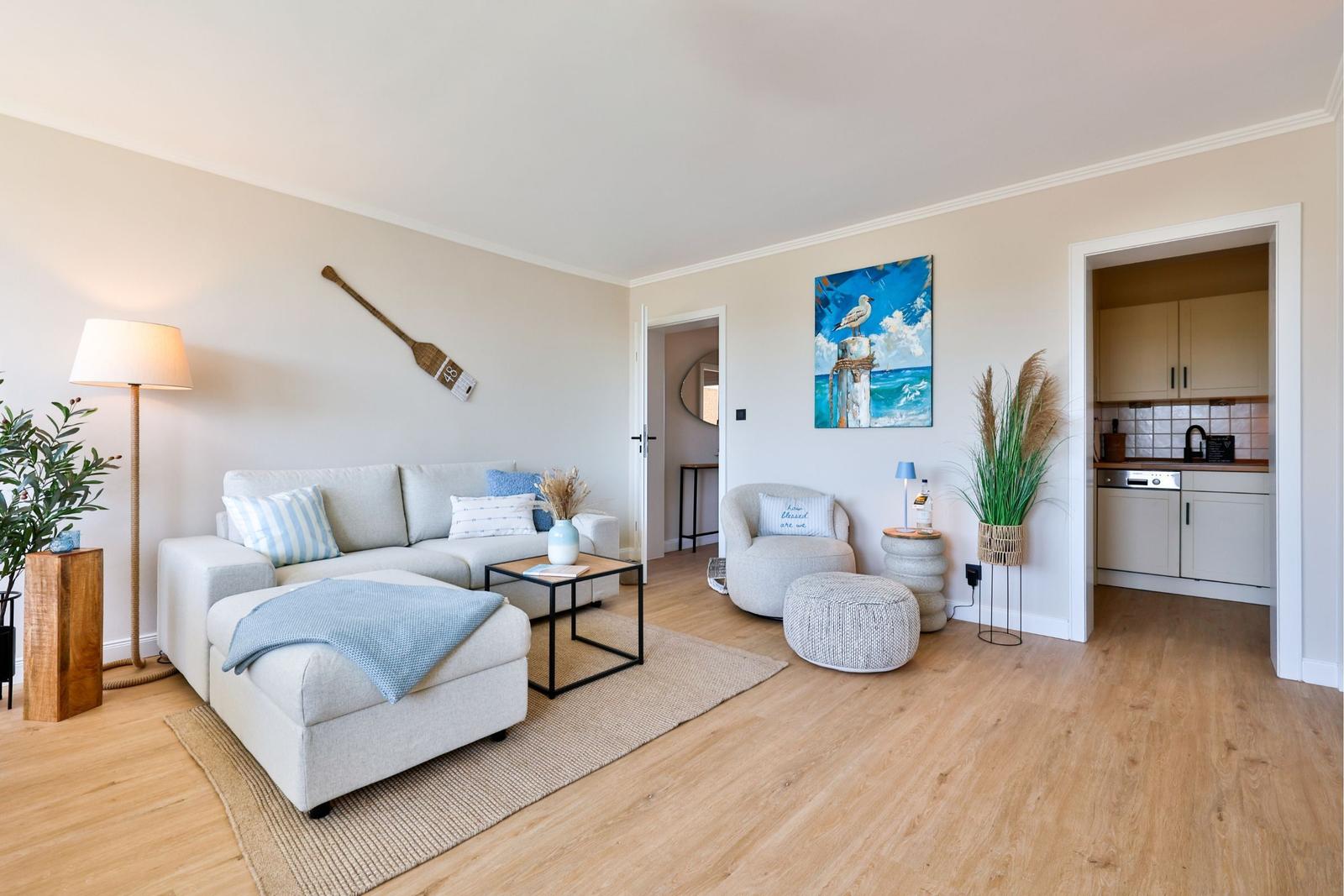 Wohnzimmer mit Sofa, Sessel und Küchenbereich. Wandbild und Segelboot-Dekoration.