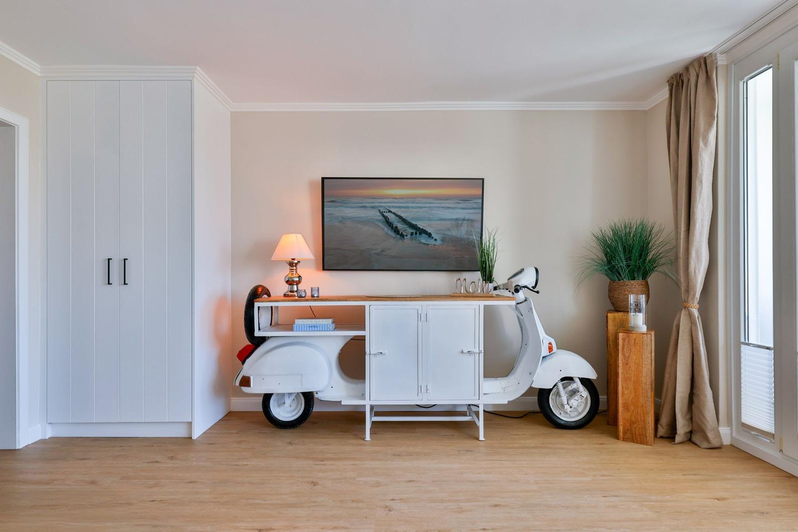 Wohnraum mit weißem Kleiderschrank, TV und Motorrad als Tisch.