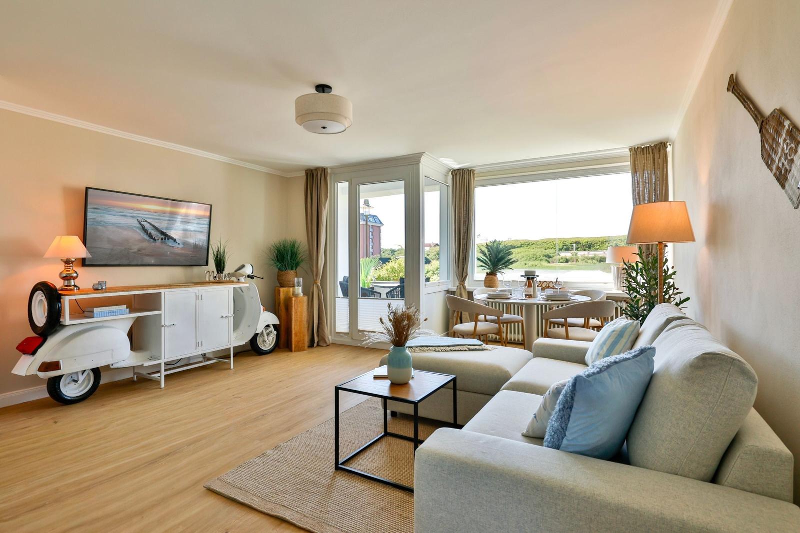 Wohnzimmer mit Sofa, Couchtisch und Blick auf Terrasse. Fernseher, Pflanzen und Motorraddekoration.
