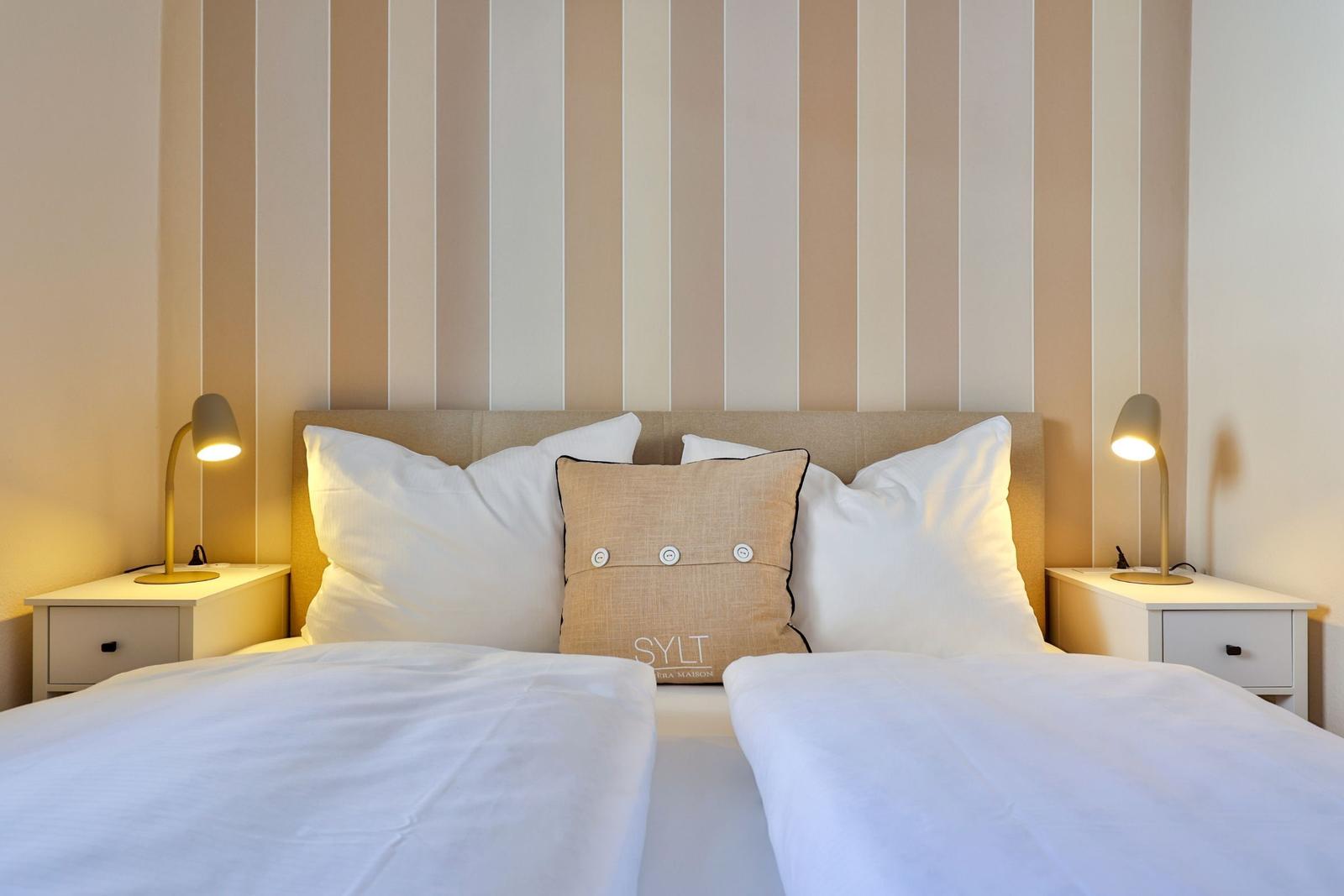 Doppelbett mit Kissen und Nachttischen mit Lampen an gestreifter Wand.