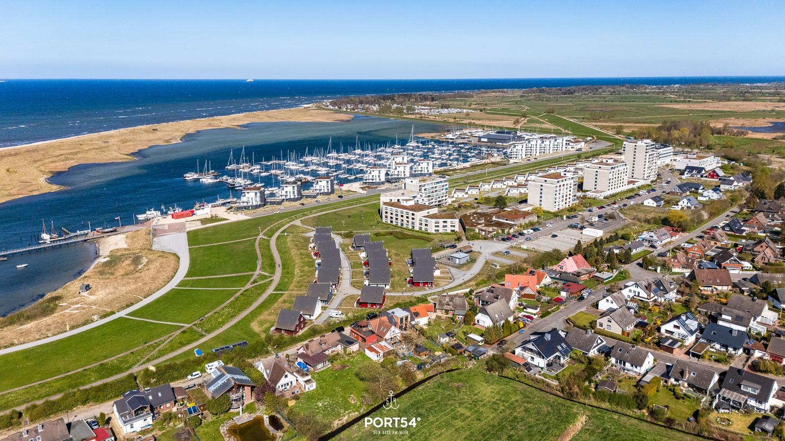 Aerial view of a coastal town with marina, residential areas, and open green spaces near the sea.
