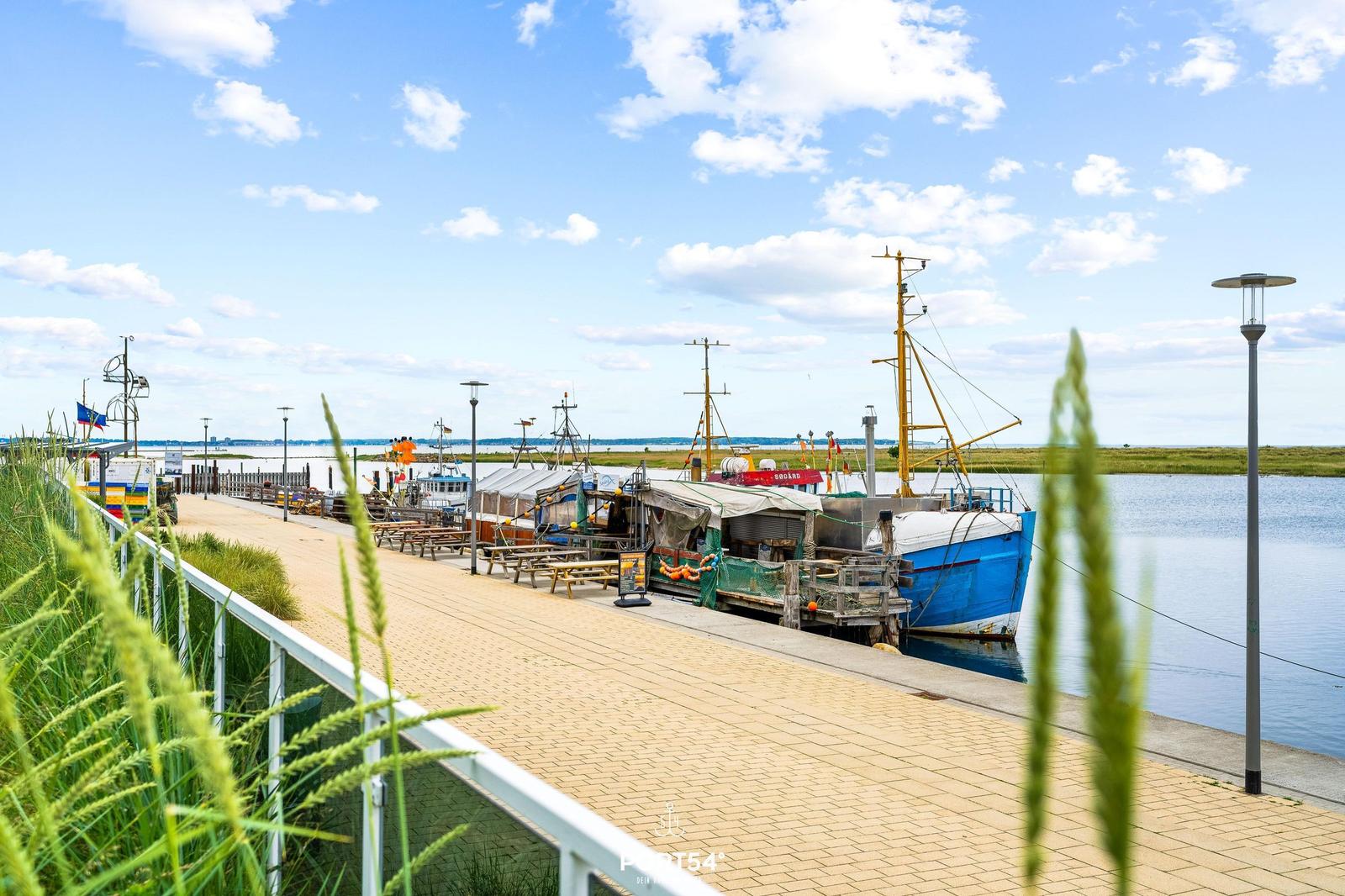 Hafenpromenade mit Booten und Picknicktischen am Wasser