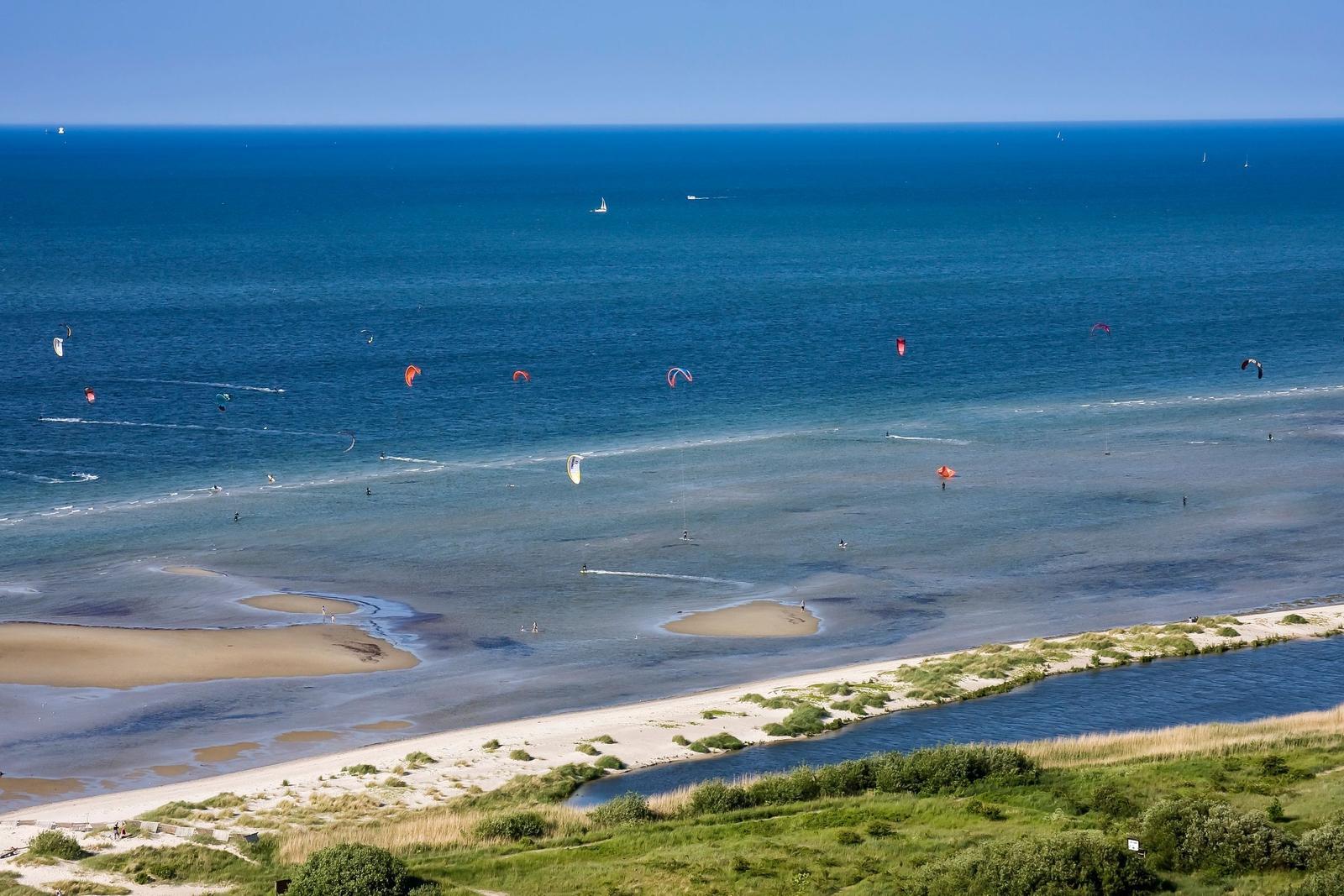 Strand mit Kitesurfern und Segelbooten im klaren Meer.