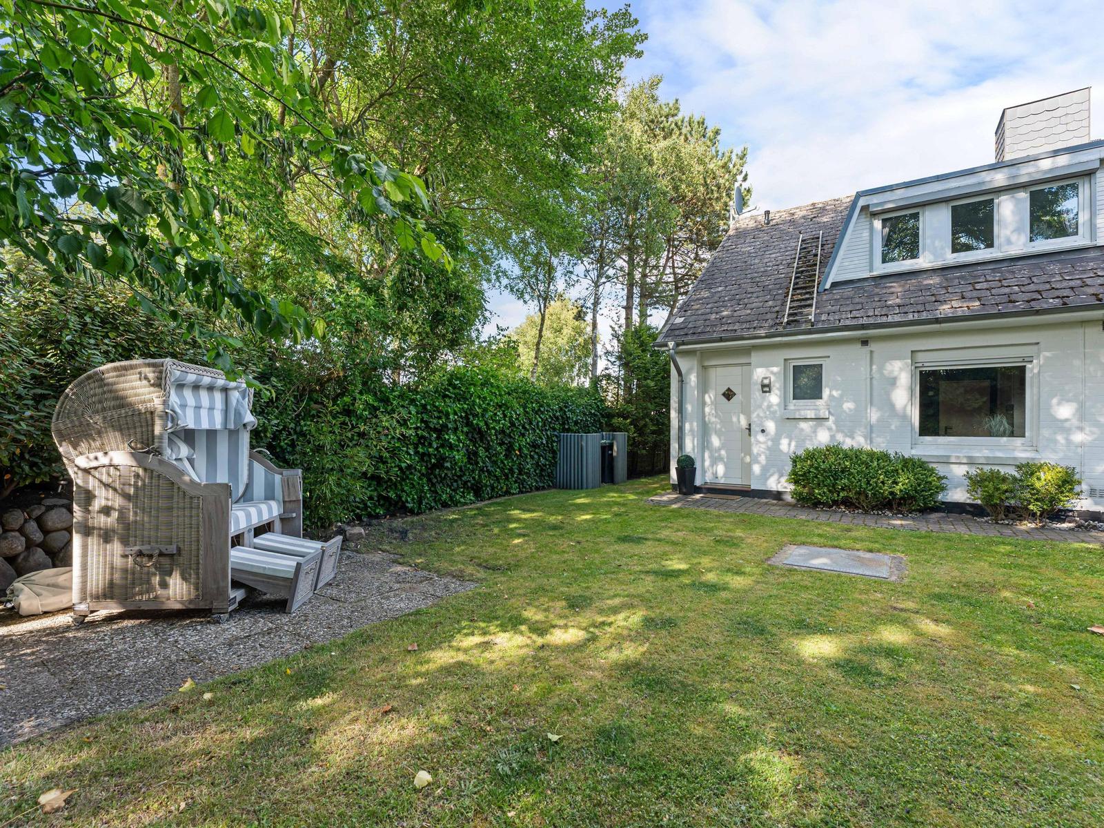 Haus mit Garten, Strandkorb und Bäumen im Hintergrund.