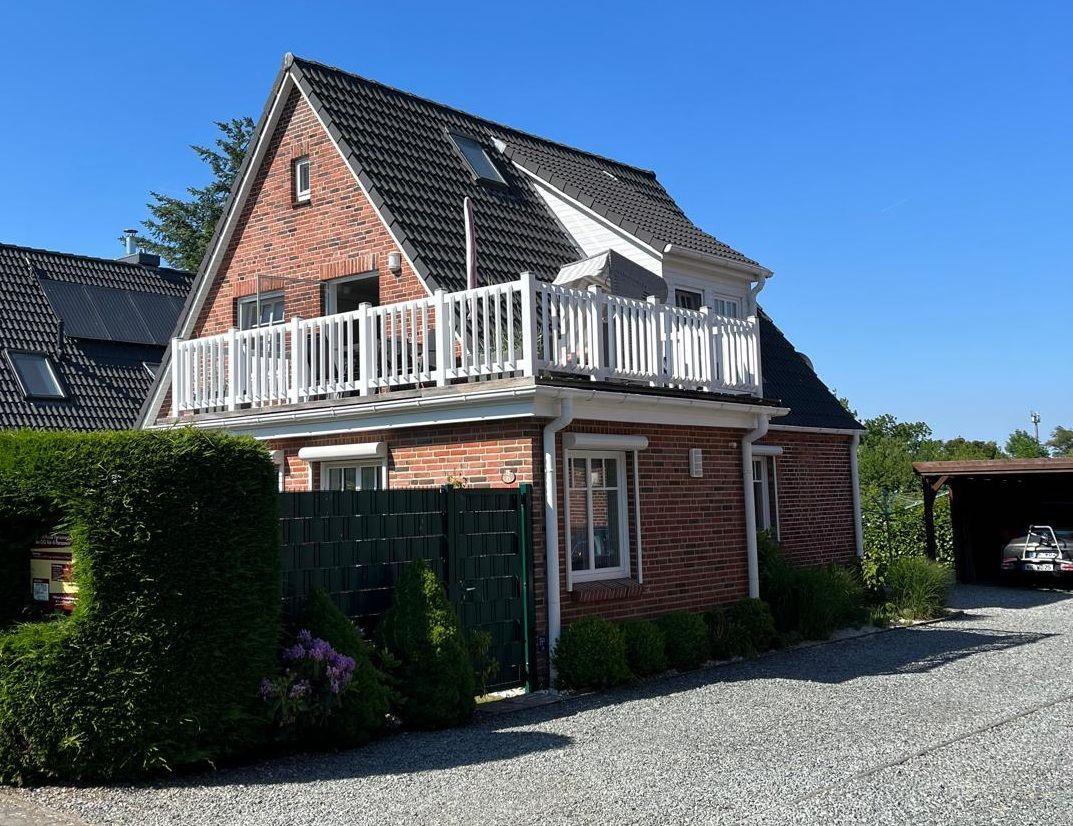 Zweistöckiges Haus mit Balkon, grüner Hecke und Kiesweg.