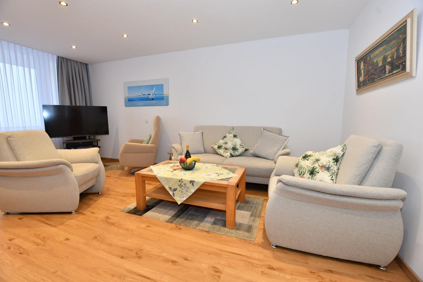 Wohnzimmer mit Sofa, Sesseln und Fernseher auf Holzboden.