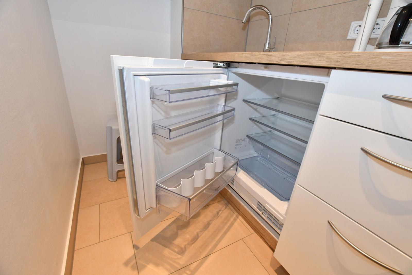 Kühlschrank mit offener Tür, transparenten Fächern und integriertem Wasserhahn