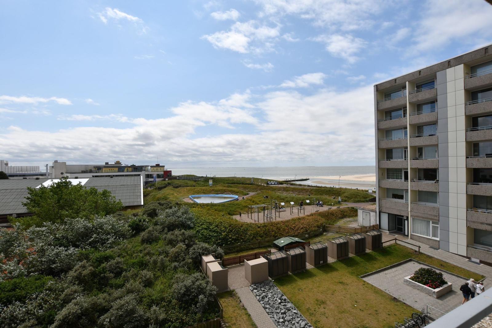 Ausblick auf Strand, Grünflächen und Wohngebäude unter blauem Himmel mit Wolken.
