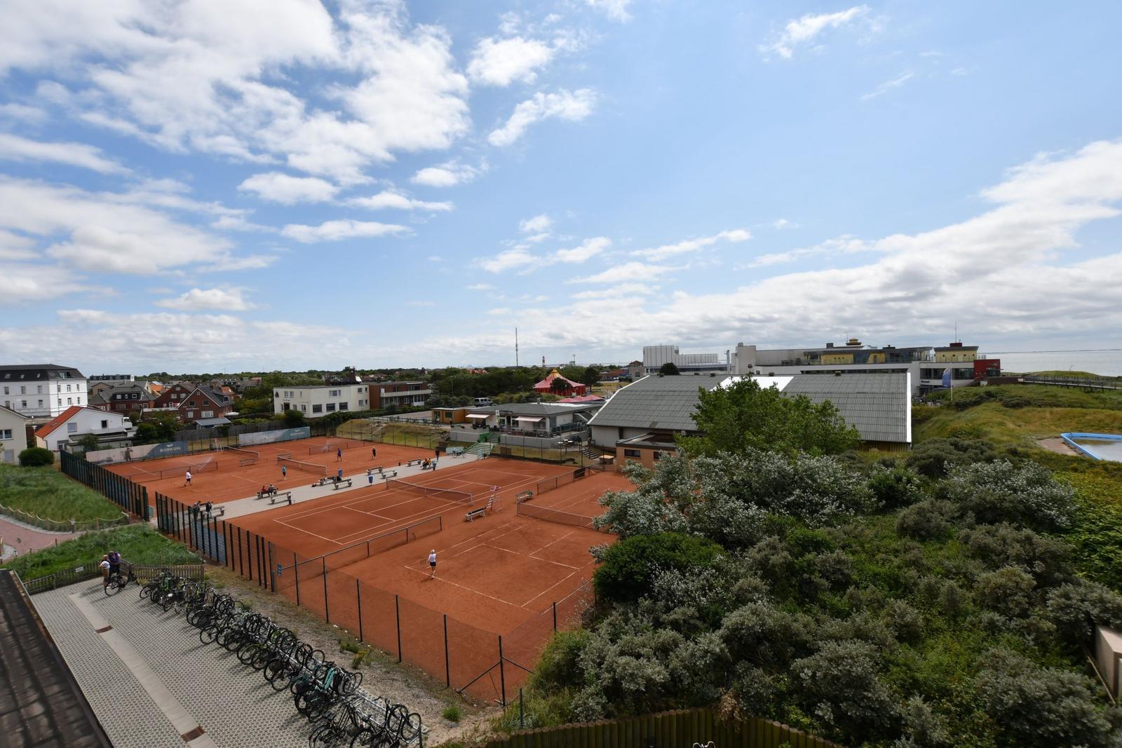 Rote Tennisplätze mit Spielern und Fahrrädern im Hintergrund.
