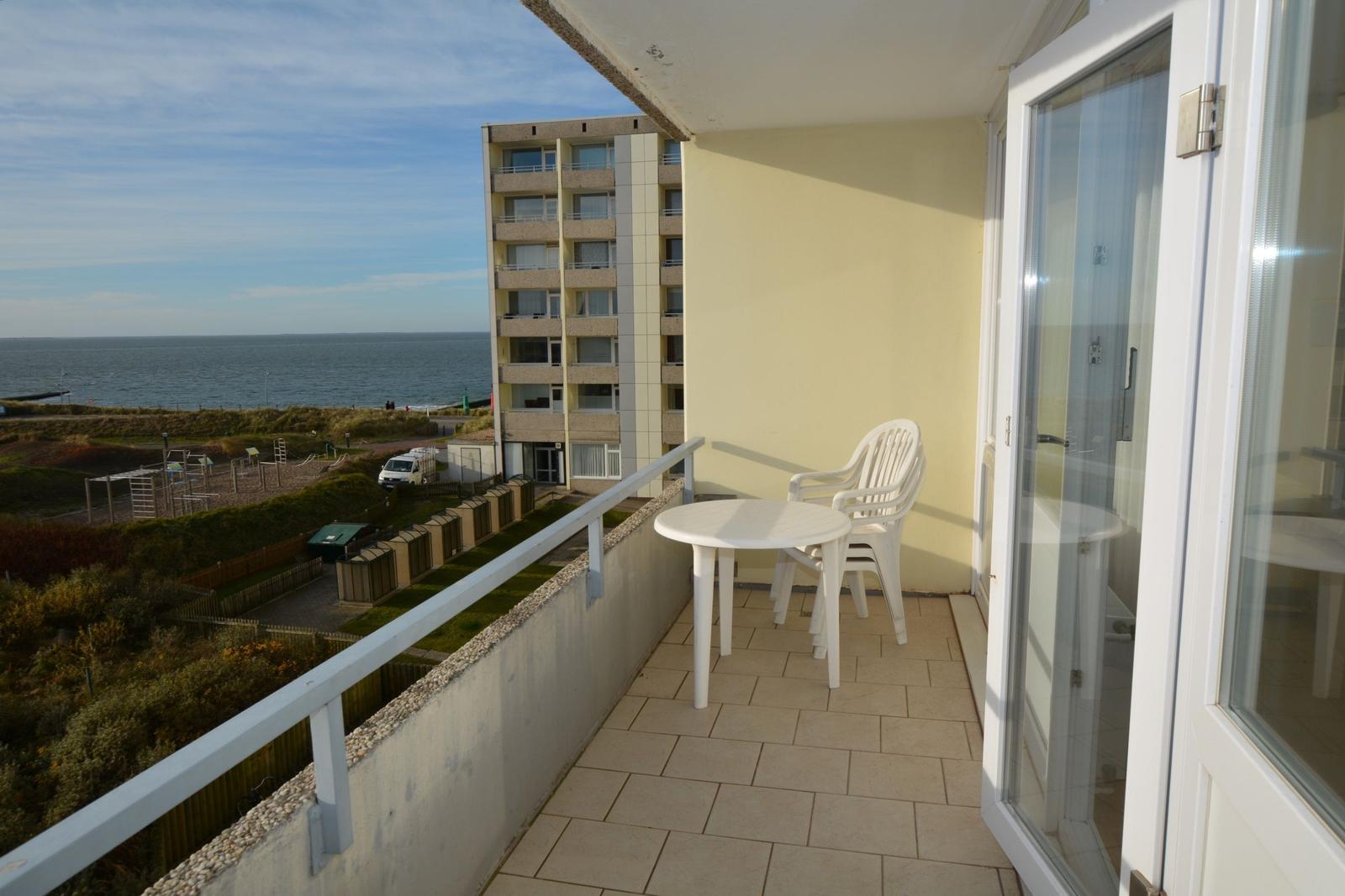 Terrasse mit Tisch und Stühlen, Blick auf Meer und Gebäude.