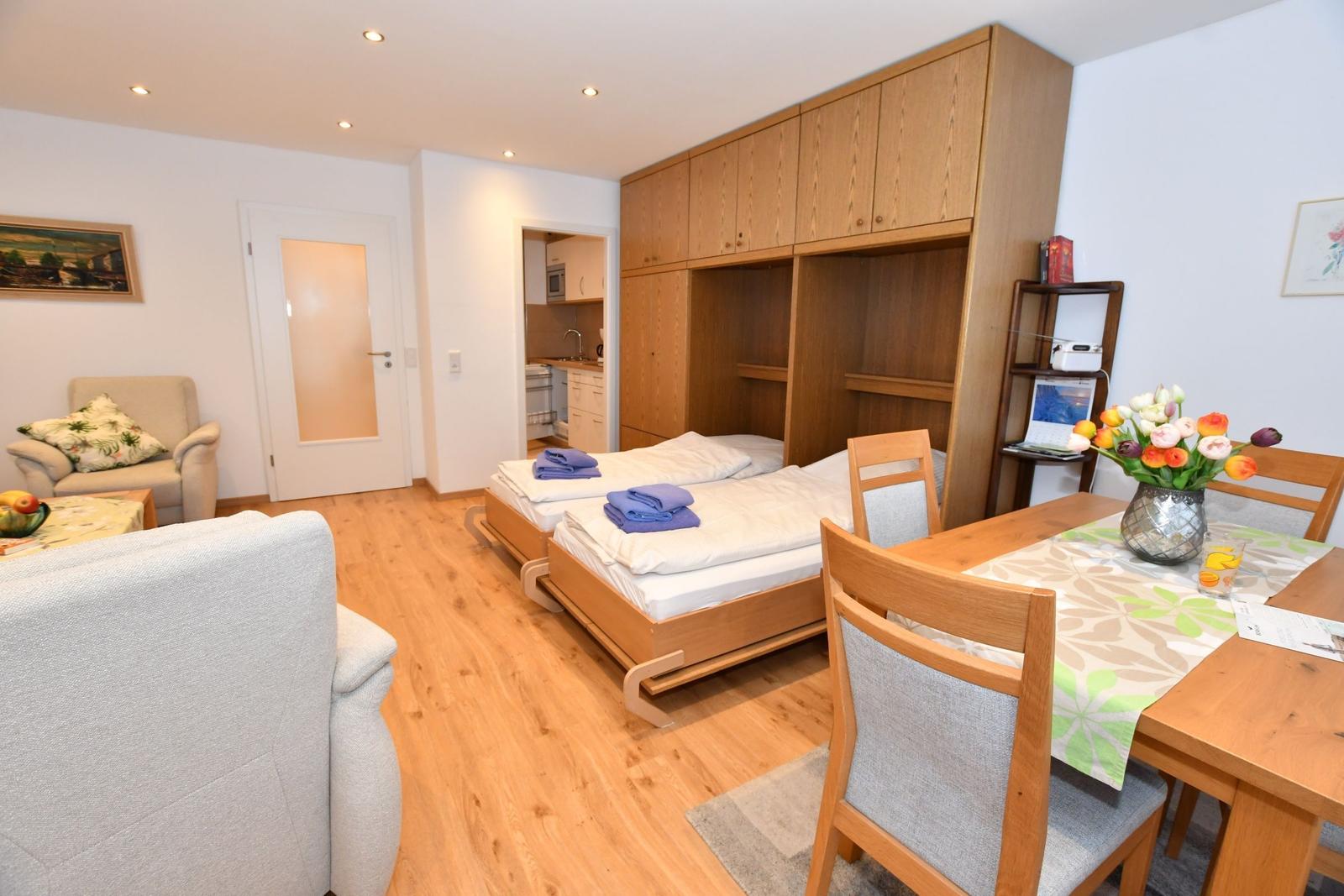 Wohnung mit Schlafgelegenheit, Esstisch und Küchenbereich im Hintergrund.