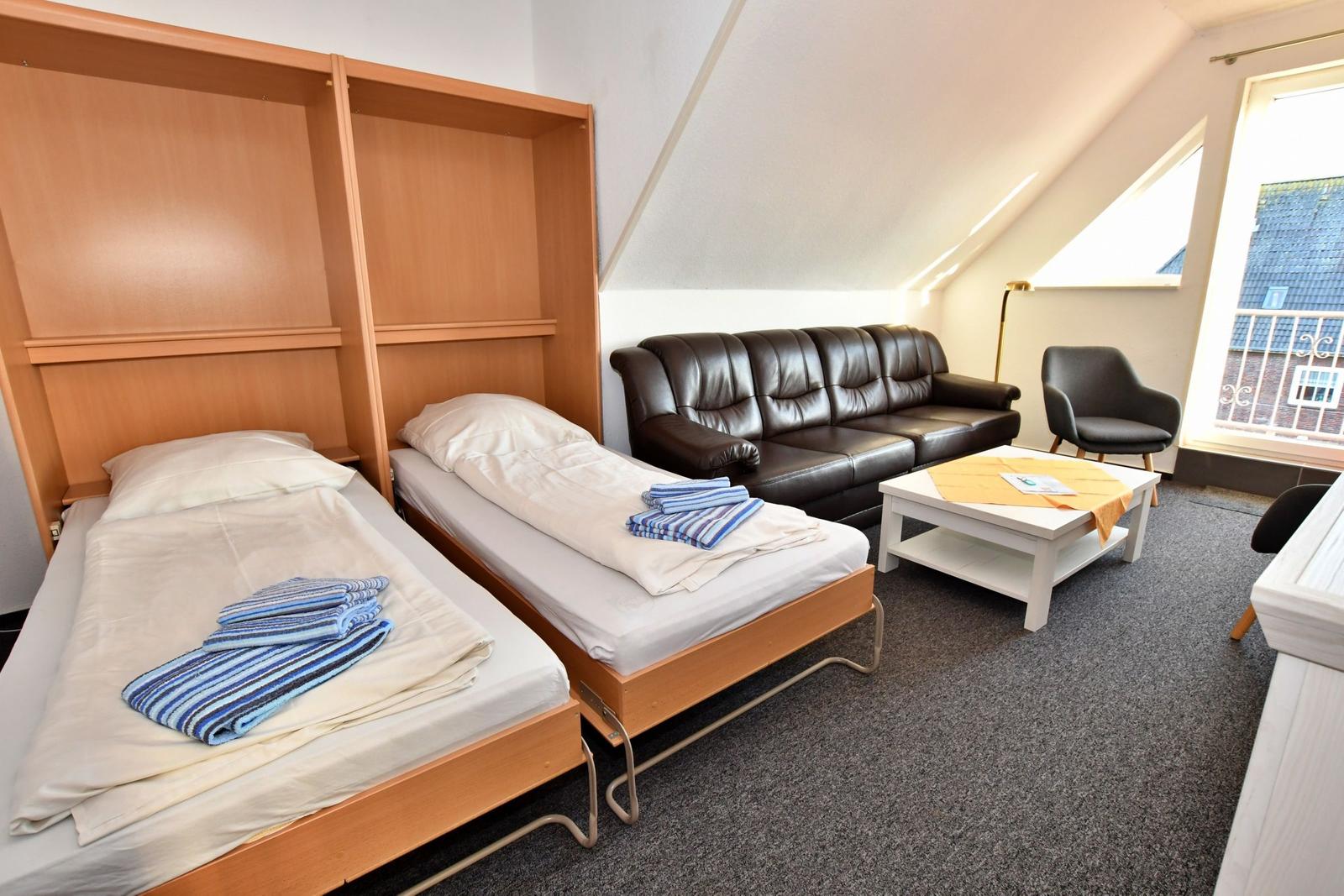 Zwei Einzelbetten mit Holzrahmen, Sofa, Sessel und Tisch in einem Dachzimmer mit Fenster.