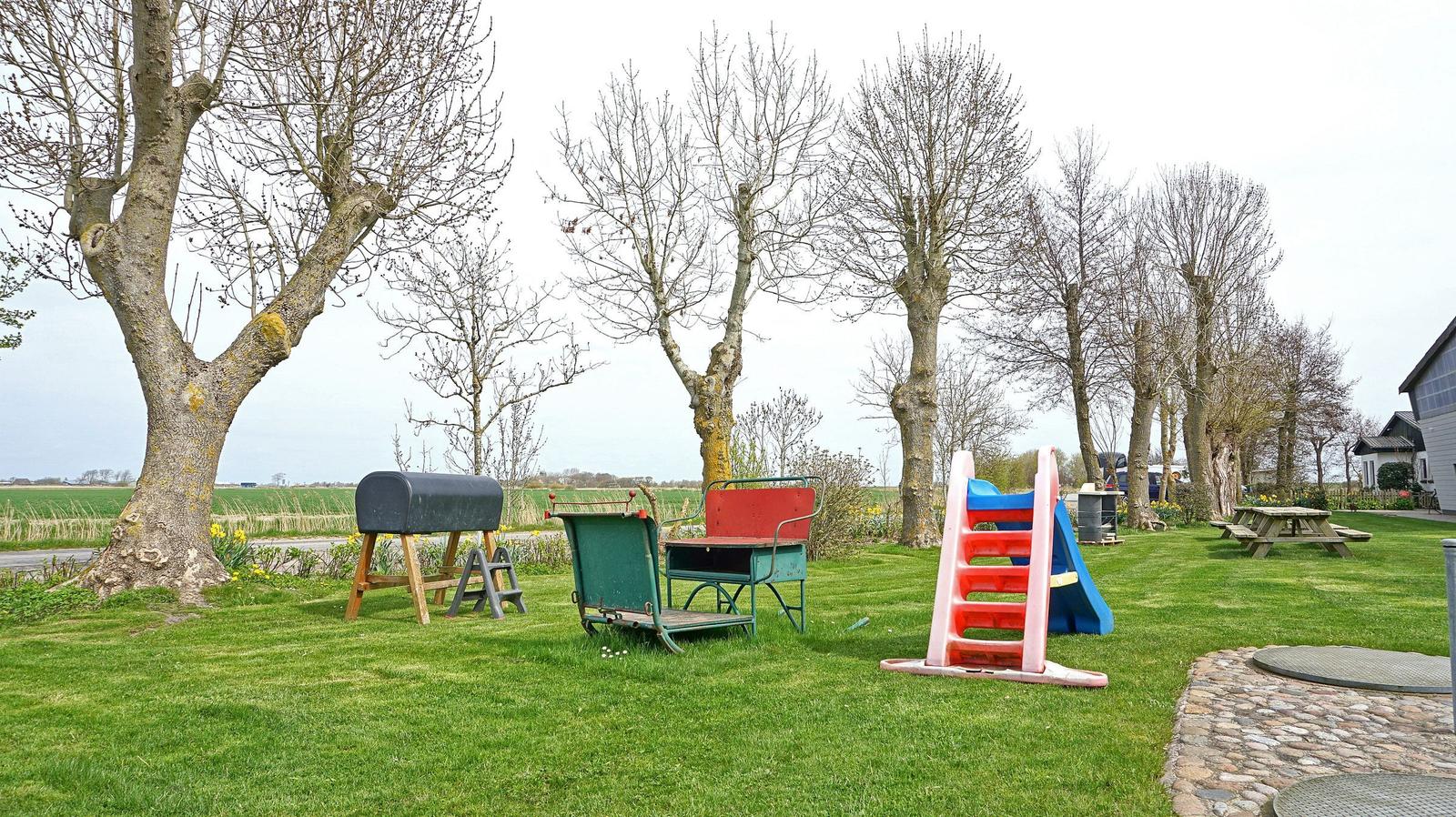 Green garden with playground, grill, and trees. Picnic table and stone path.