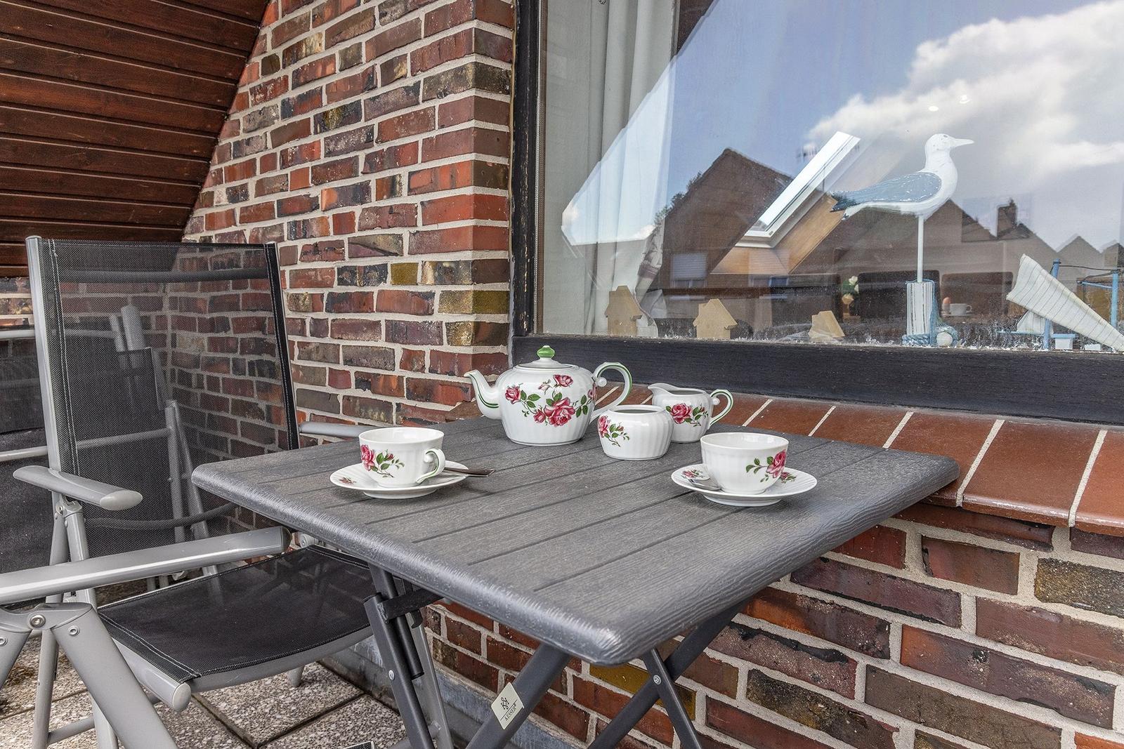 Terrasse mit Tisch, Stühlen und Teeservice vor Backsteinwand und Fenster