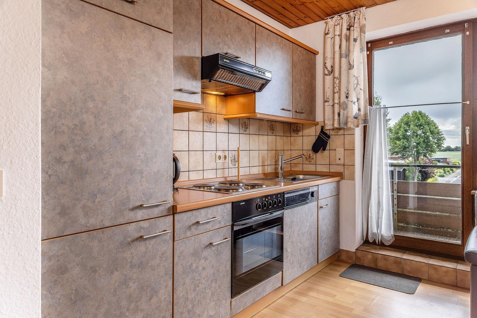 Küche mit Dunstabzug, Herd und Backofen. Balkon mit Blick auf Grünflächen.