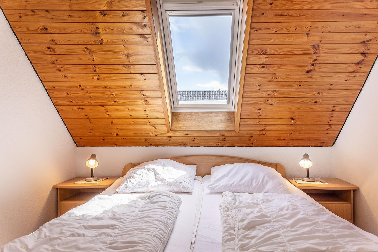 Schlafzimmer mit Dachfenster, Holzdecke und zwei Nachttischen mit Lampen.