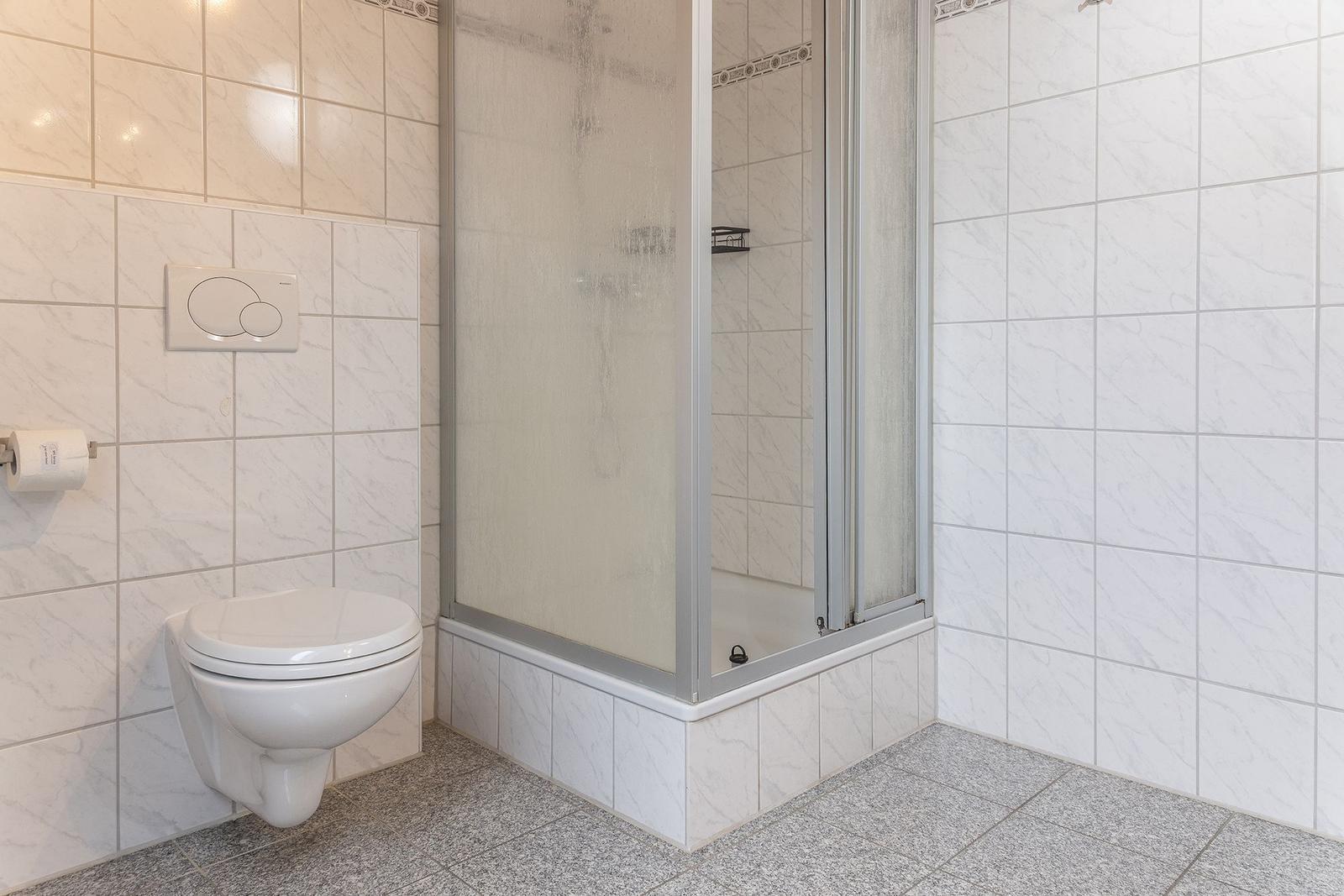 Badezimmer mit Dusche, Toilette und Fliesen