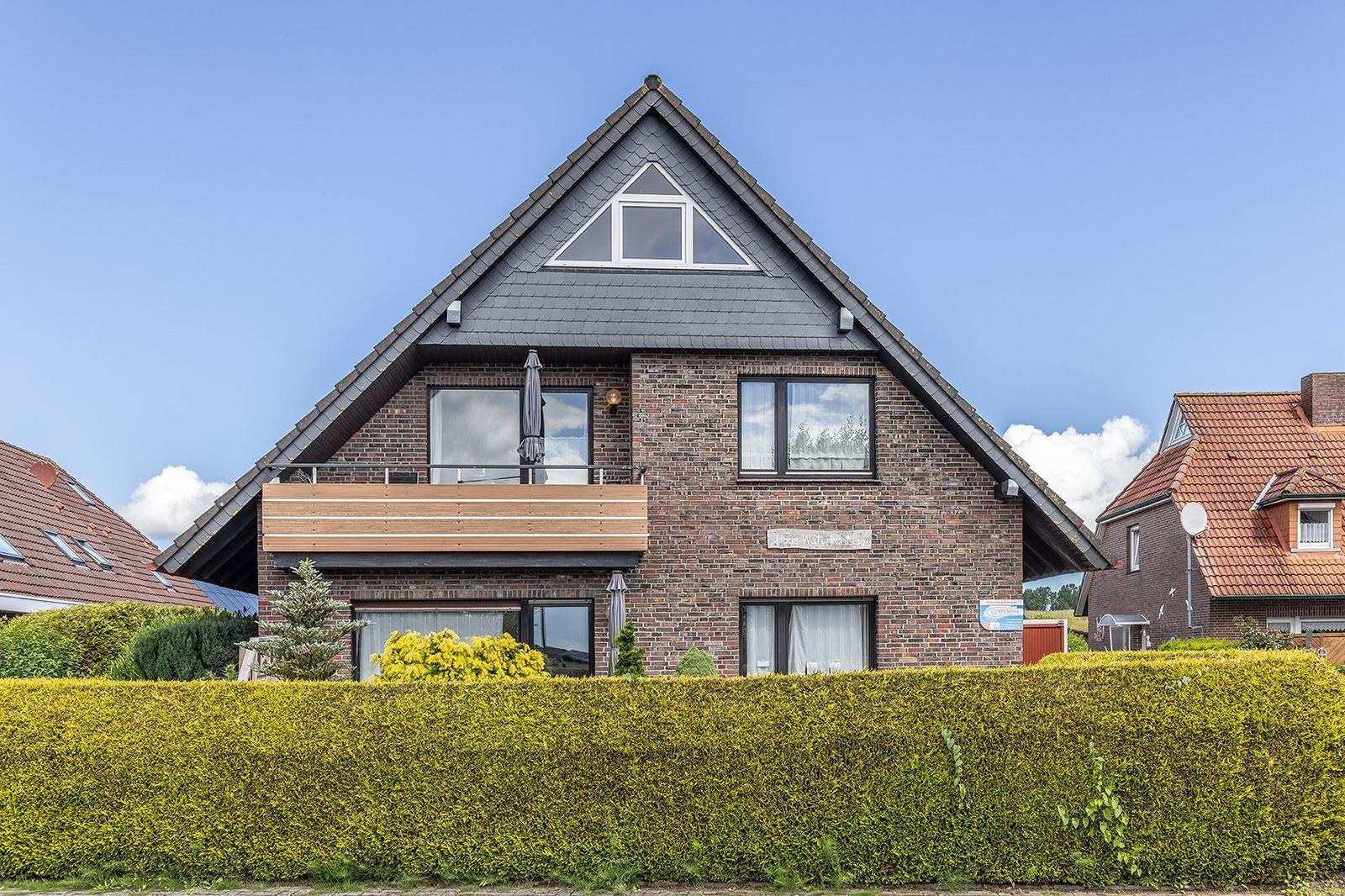 Zweistöckiges Haus mit Balkon, Holzveranda und grünem Heckenzaun.
