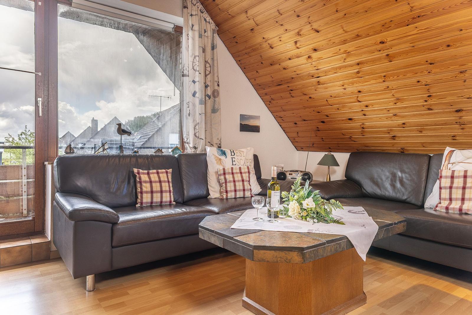 Wohnzimmer mit Ledersofa, Holzdecke und Blick auf Balkon.