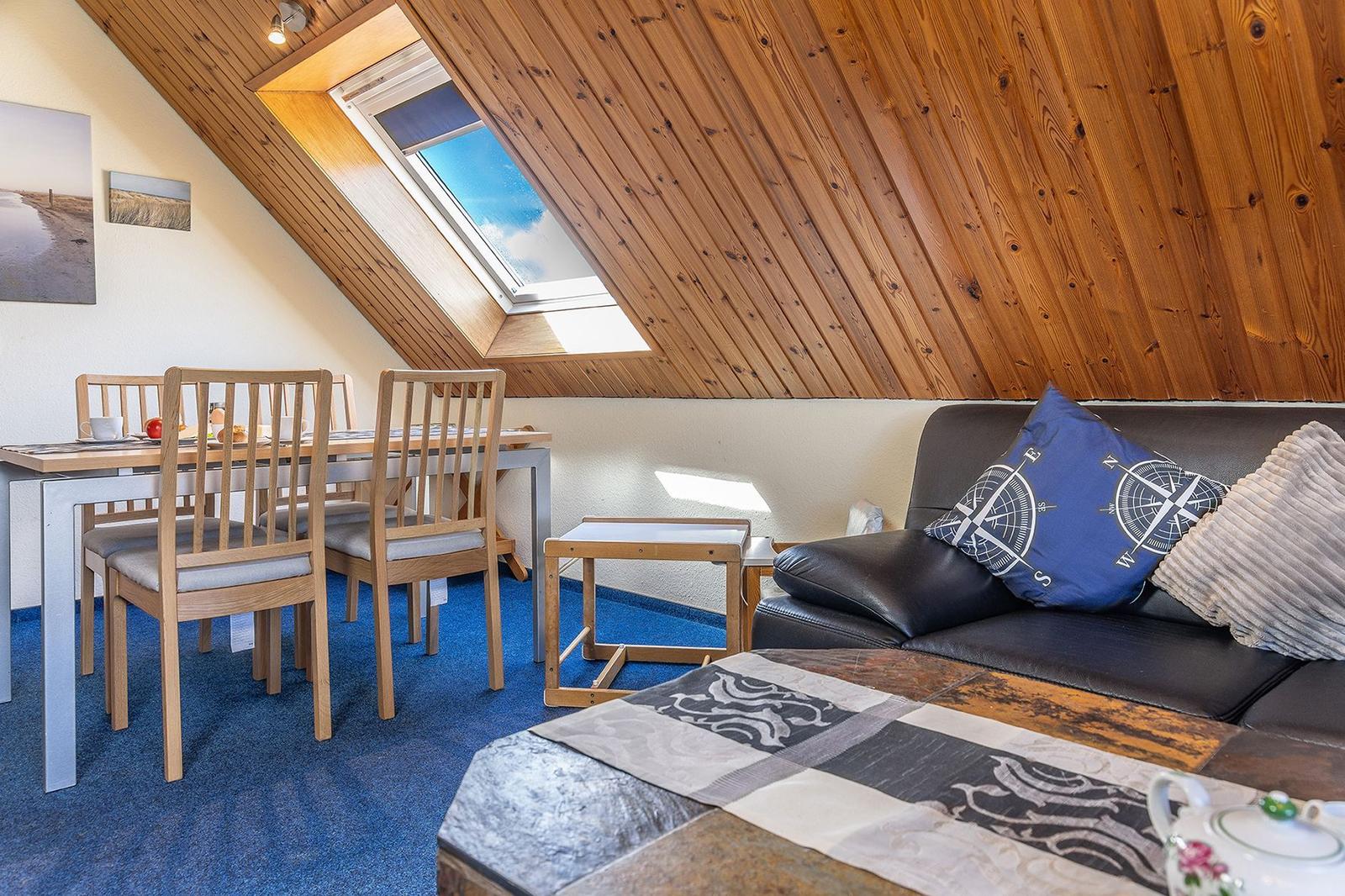 Wohn- und Essbereich mit Holzdecke, Dachfenster und Sofa mit Kissen.