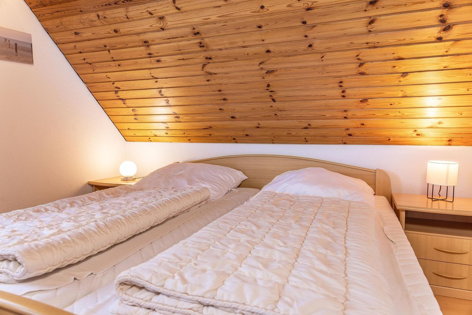 Zimmer mit Doppelbett, Holzdecke und Nachttischen mit Lampen.