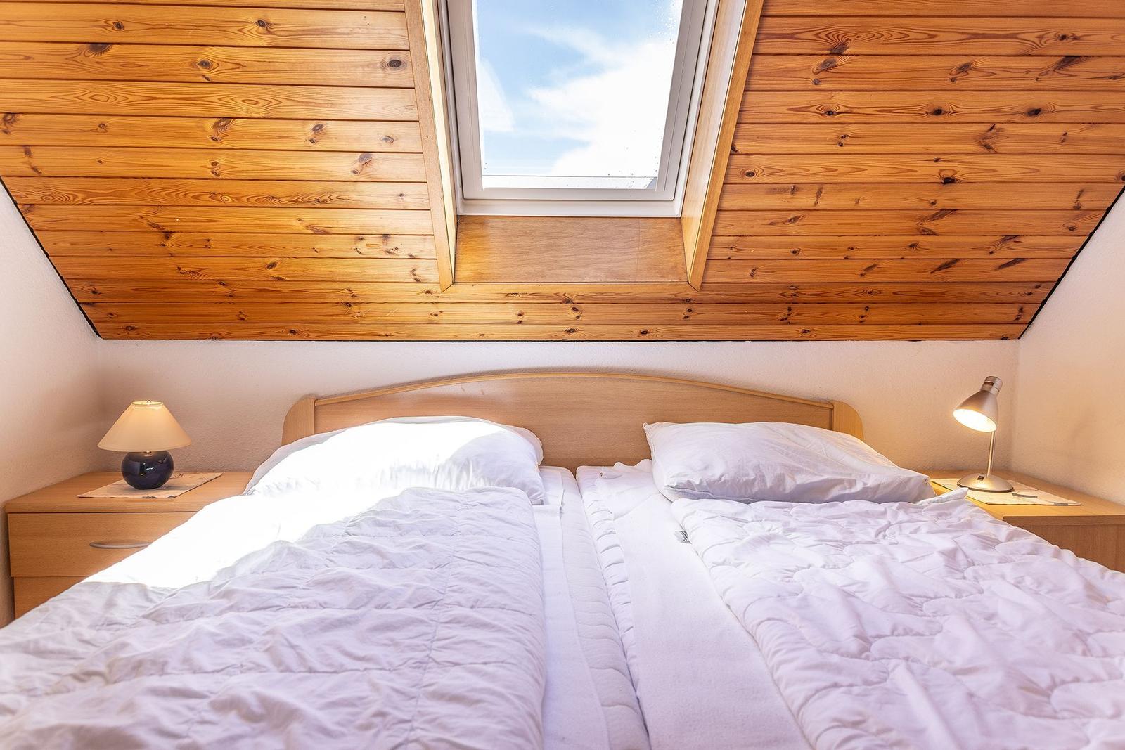Doppelbett unter Holzdecke mit Dachfenster und Nachttischen