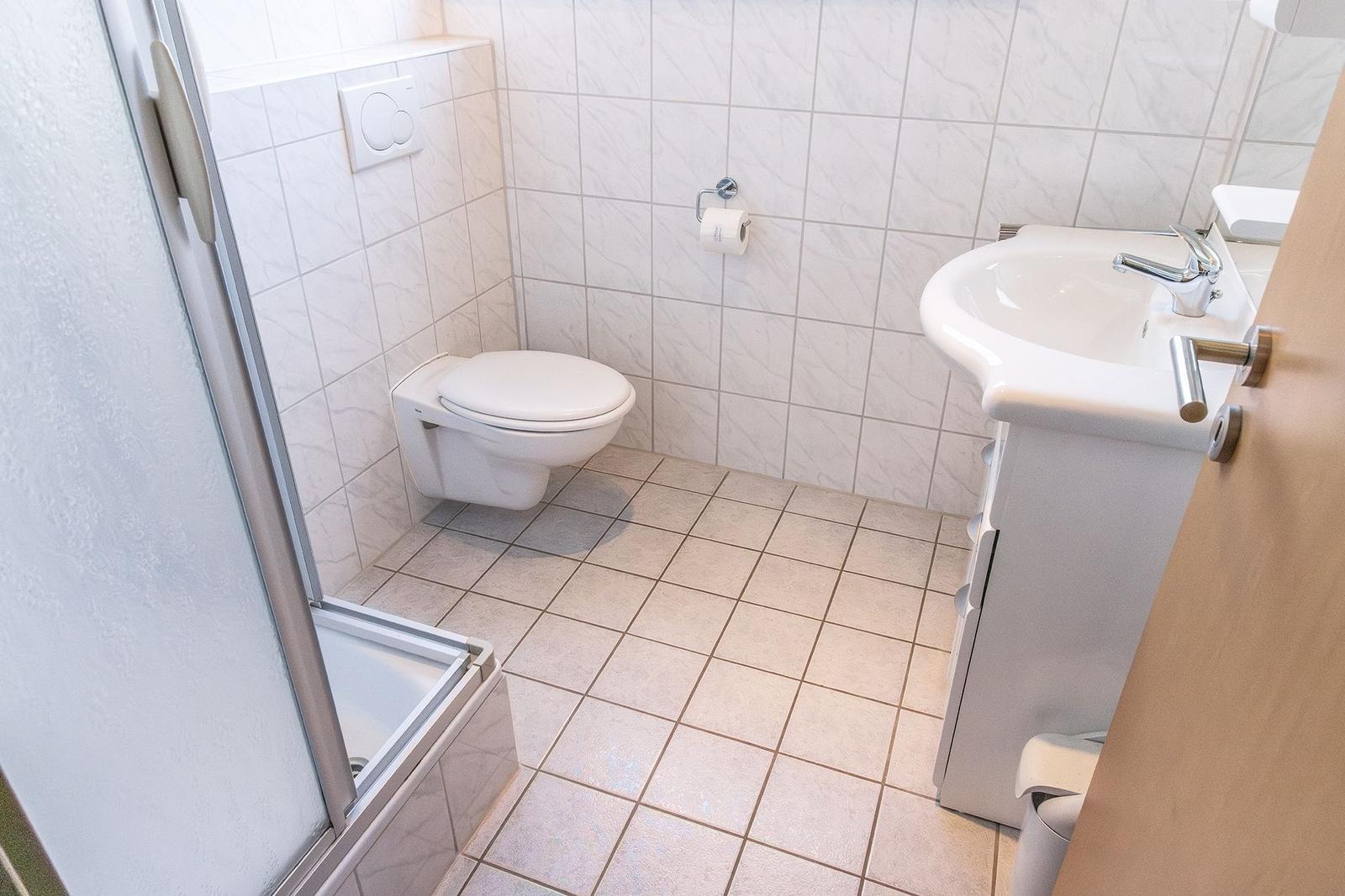 Badezimmer mit Toilette, Waschbecken und Dusche. Fliesenwand und -boden.