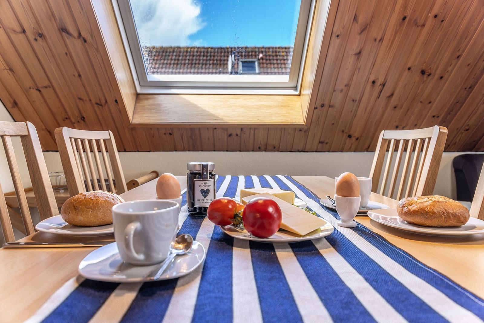 Frühstückstisch mit Käse, Tomaten, Eiern und Brot unter einem Dachfenster mit Holzdecke.