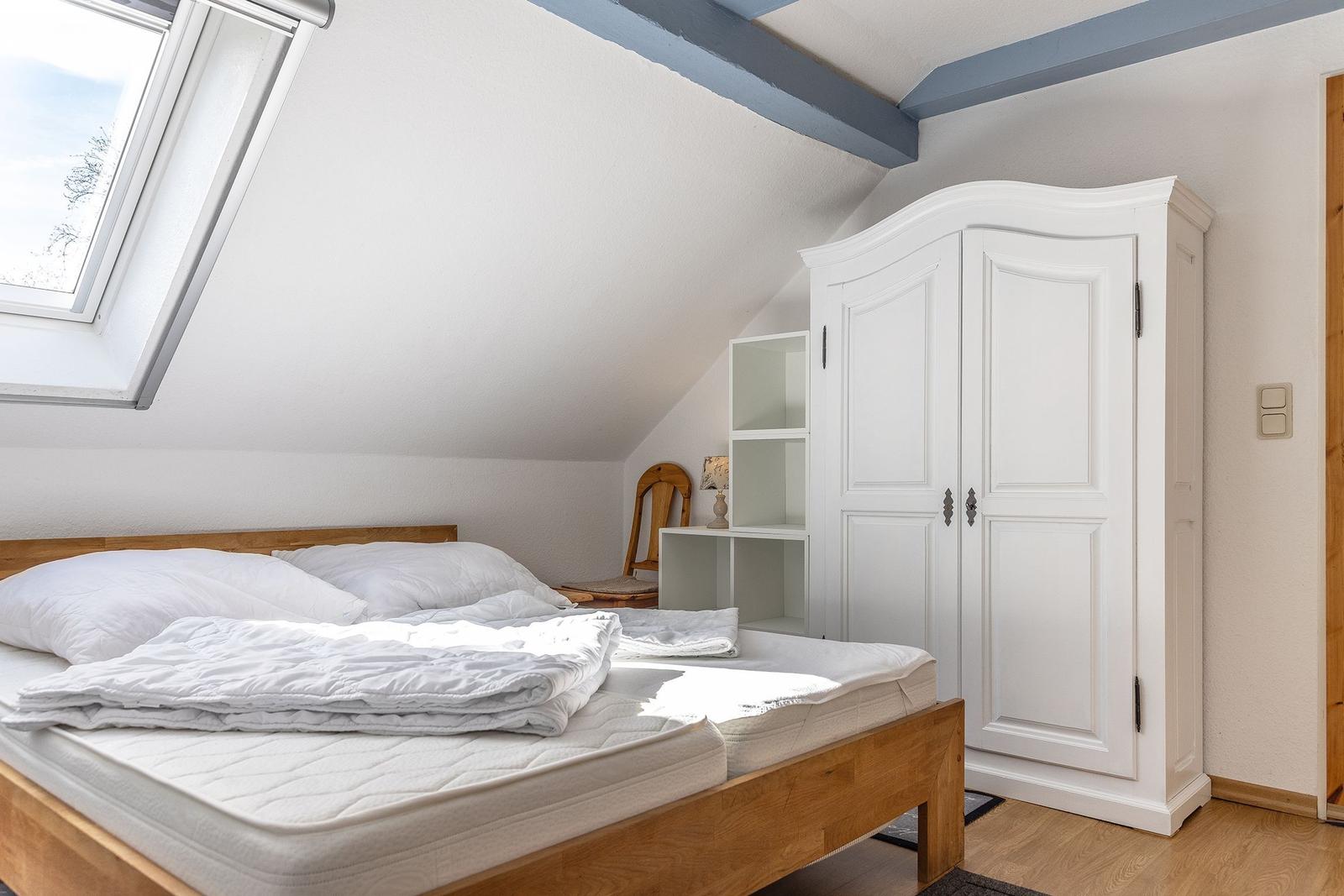 Schlafzimmer mit Dachschrägen, Dachfenster, weißem Schrank und Holzbett.