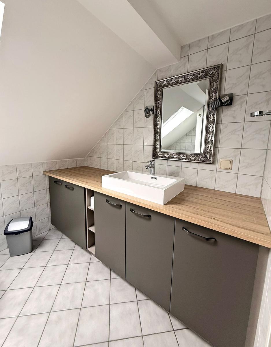 Bad mit Waschtisch, Spiegel und Holzoberfläche an schräger Wand.