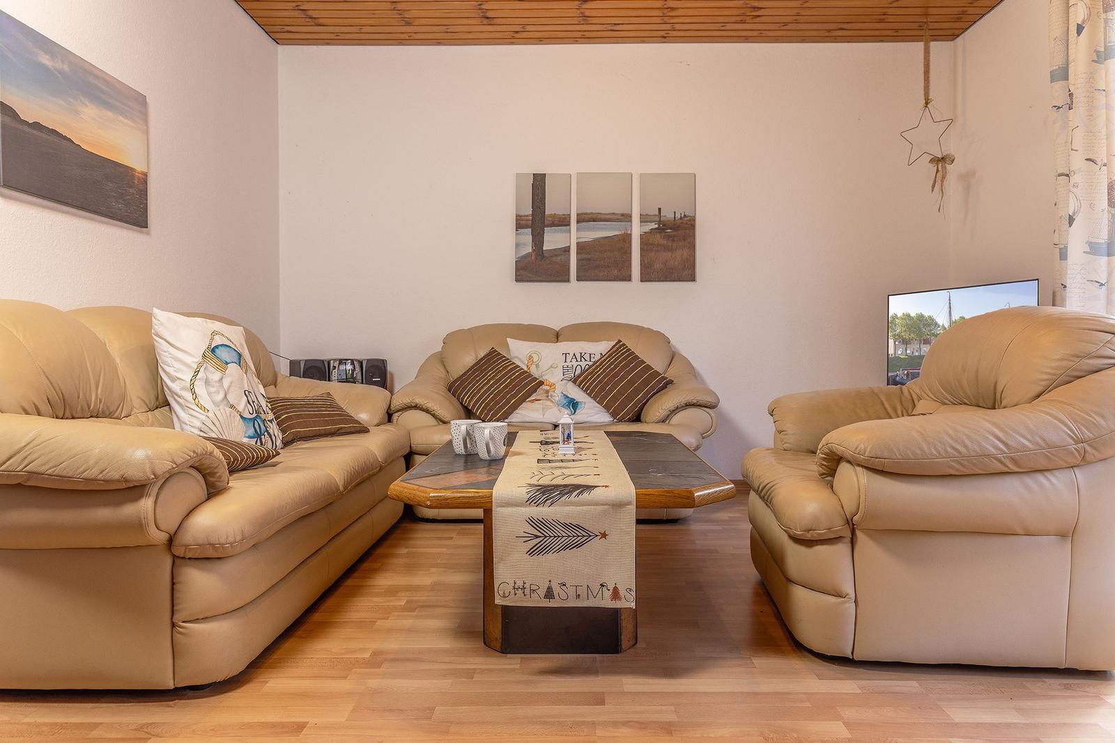 Wohnzimmer mit beigen Ledermöbeln, Holzboden und Fernseher.