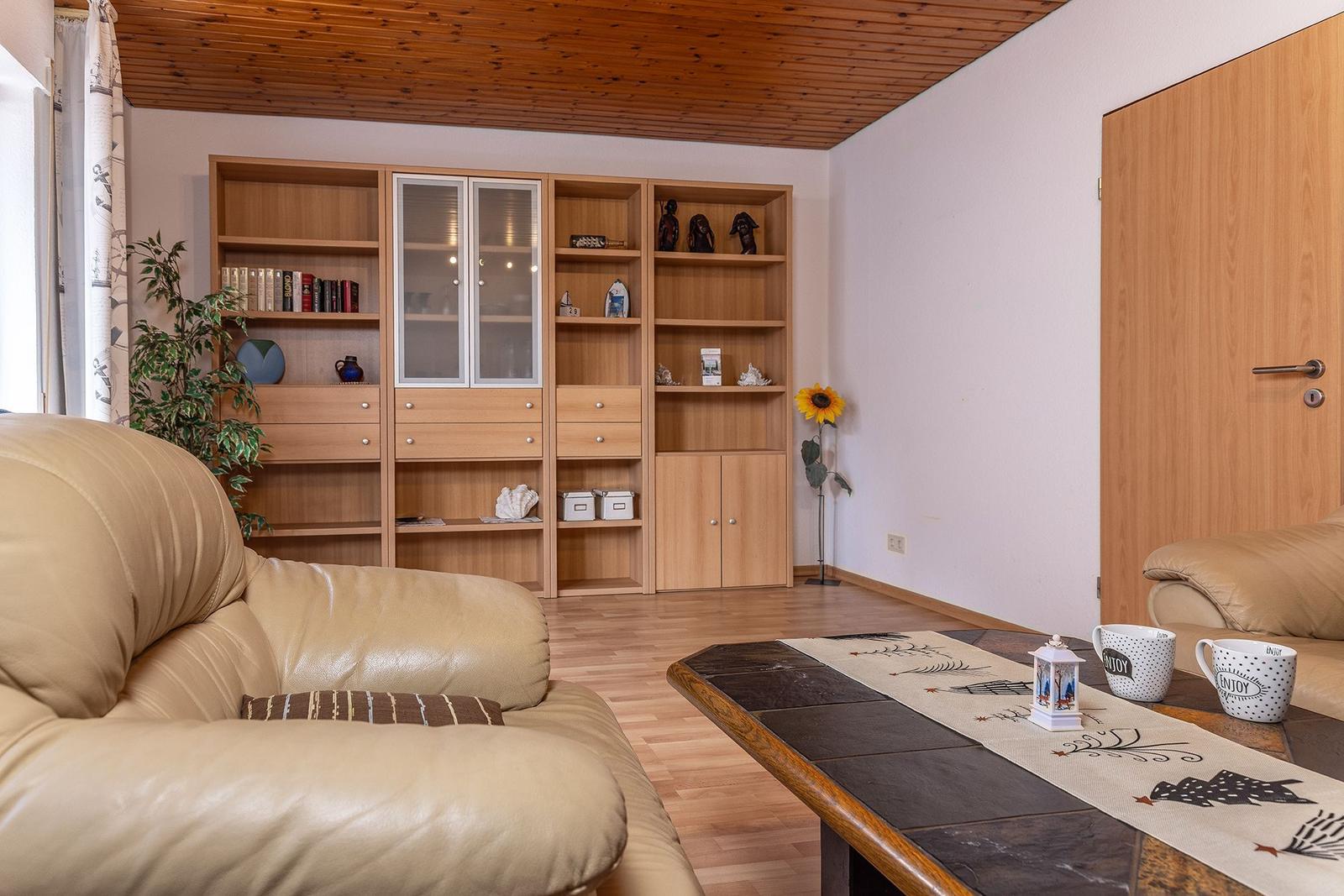 Wohnzimmer mit Ledersofa, Holzregal und Tisch mit Tischläufer.