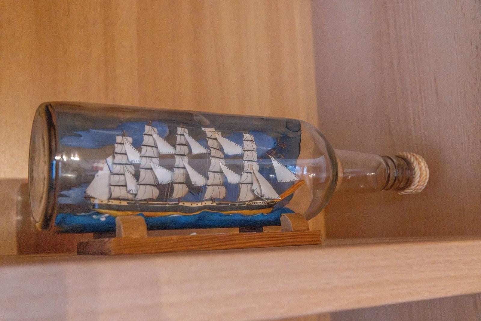 Ein Schiffmodell in einer Glasflasche auf einem Holzgestell.