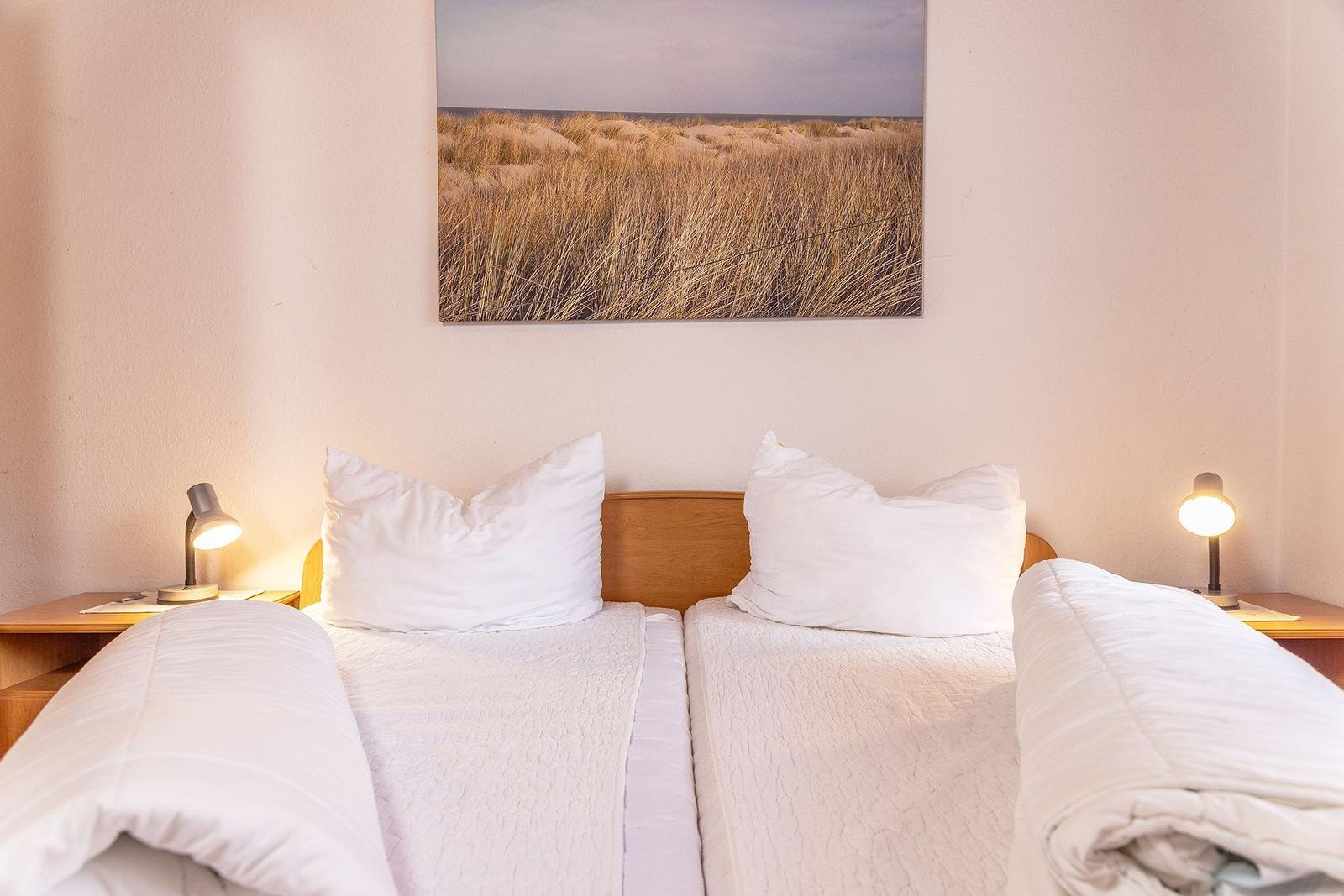 Zwei Betten mit weißen Kissen und Decken unter einem Strandbild an der Wand.