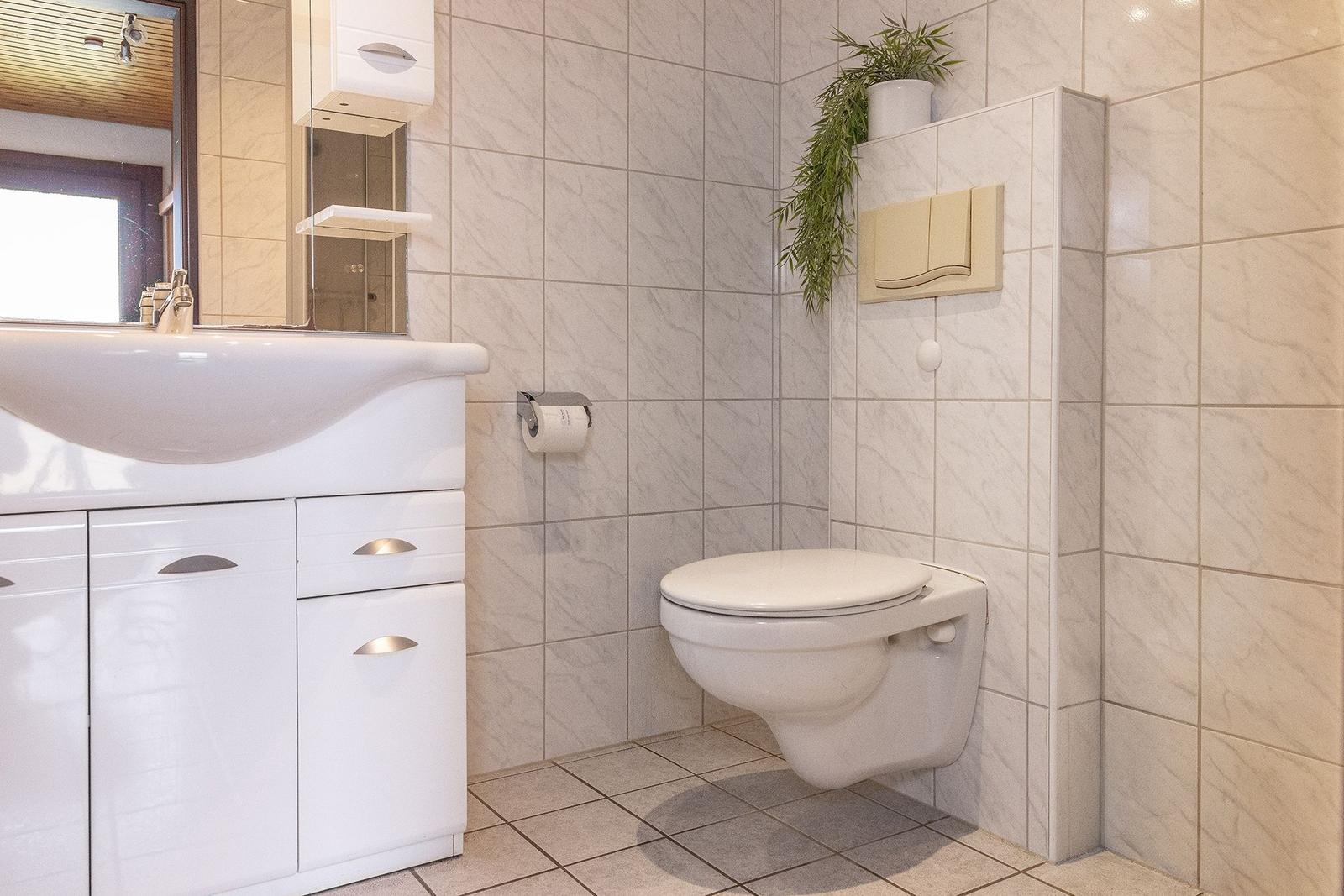 Badezimmer mit Waschbecken, Spiegel, Toilette und Pflanze an der Wand.