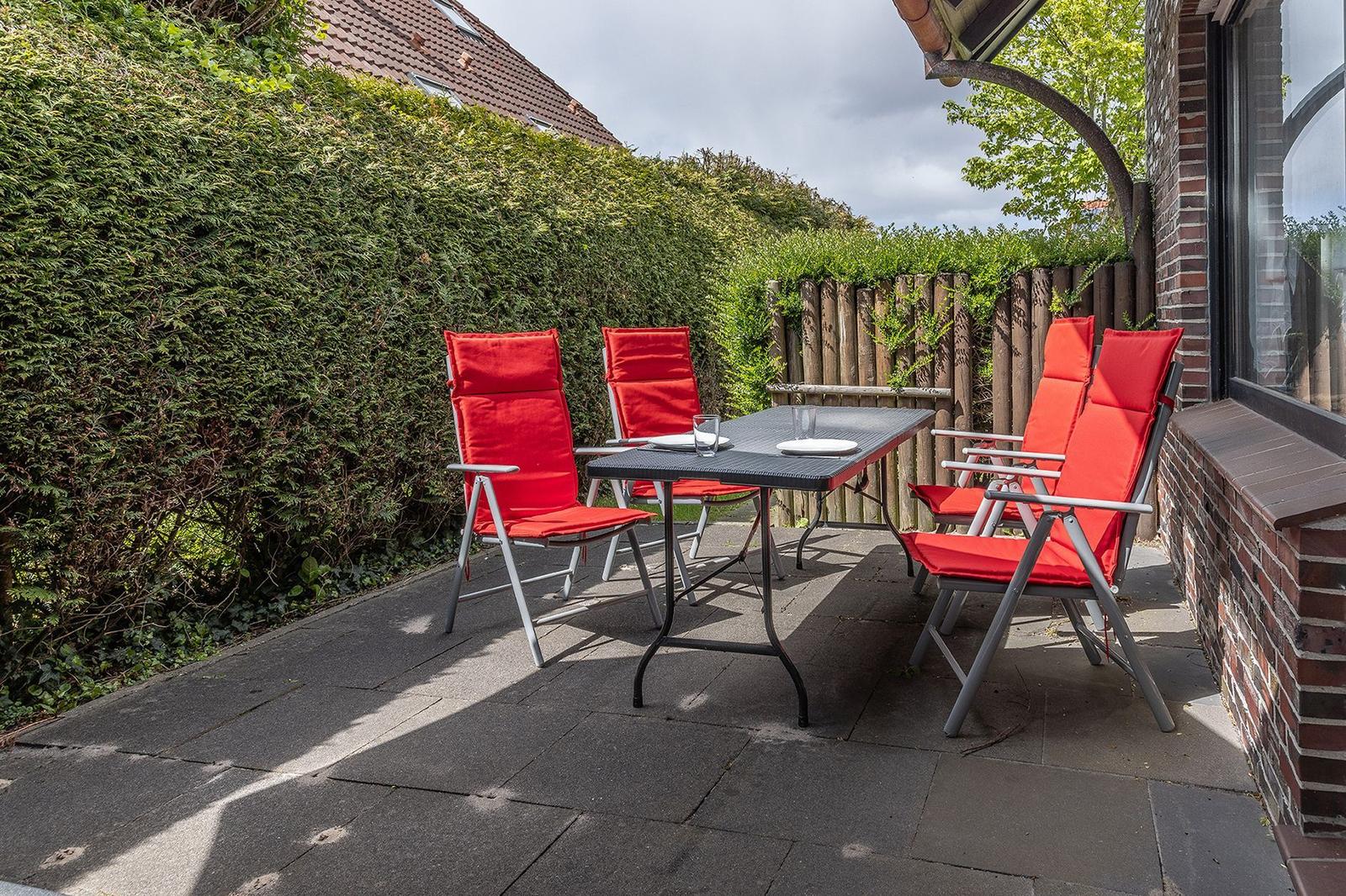 Terrasse mit roten Stühlen und Tisch, umgeben von Hecke und Zaun.