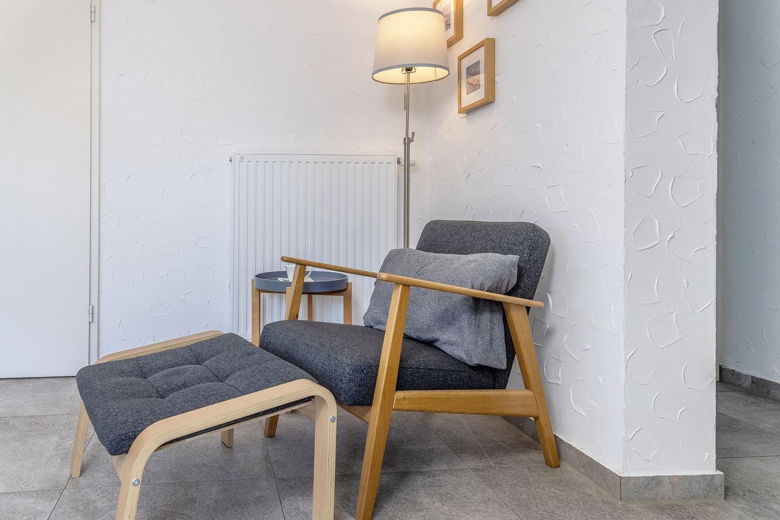 Ein Sessel mit Fußhocker und Stehlampe an der Wand.