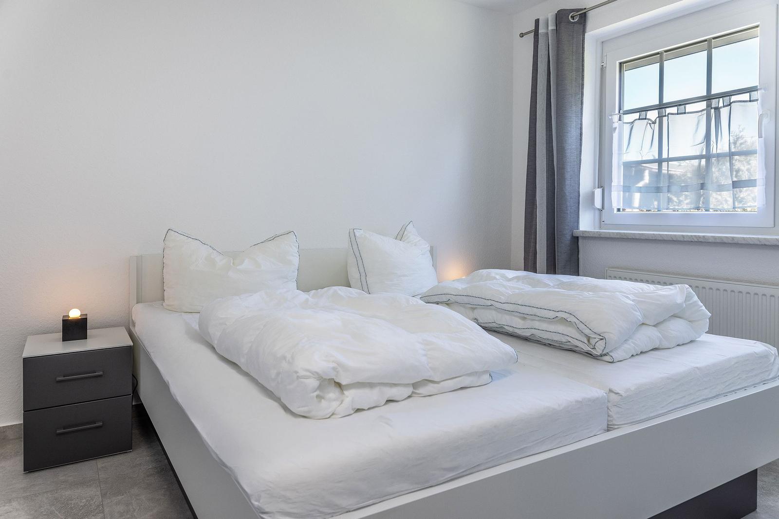 Schlafzimmer mit Doppelbett, Nachttisch und Fenster mit Vorhängen.