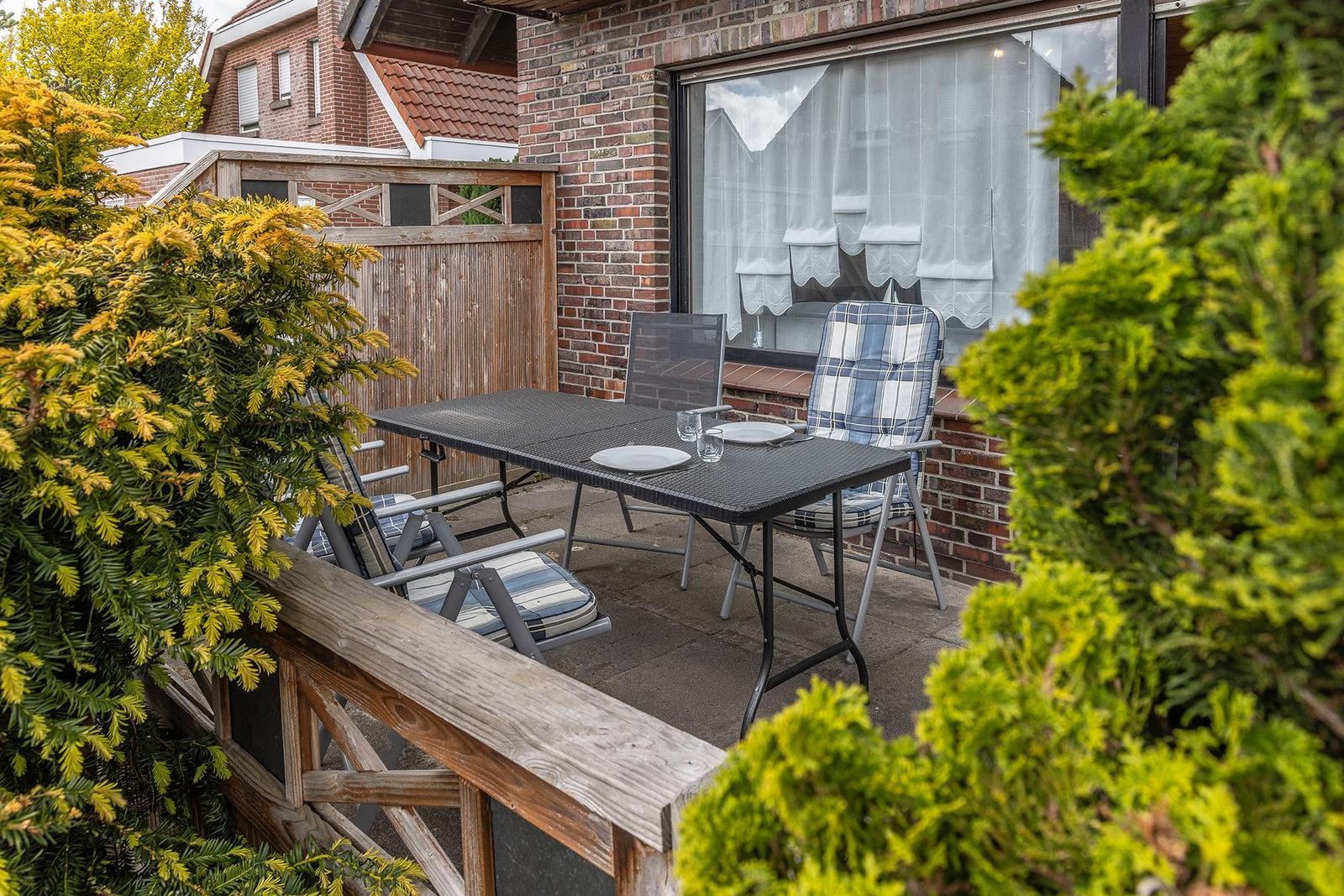 Terrasse mit Tisch, Stühlen und Garten. Holzgeländer und grüne Pflanzen umgeben den Außenbereich.