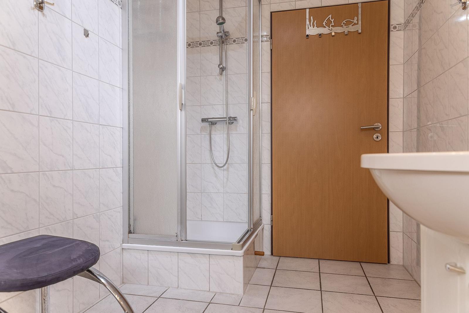 Badezimmer mit Dusche, Waschbecken und Stuhl.