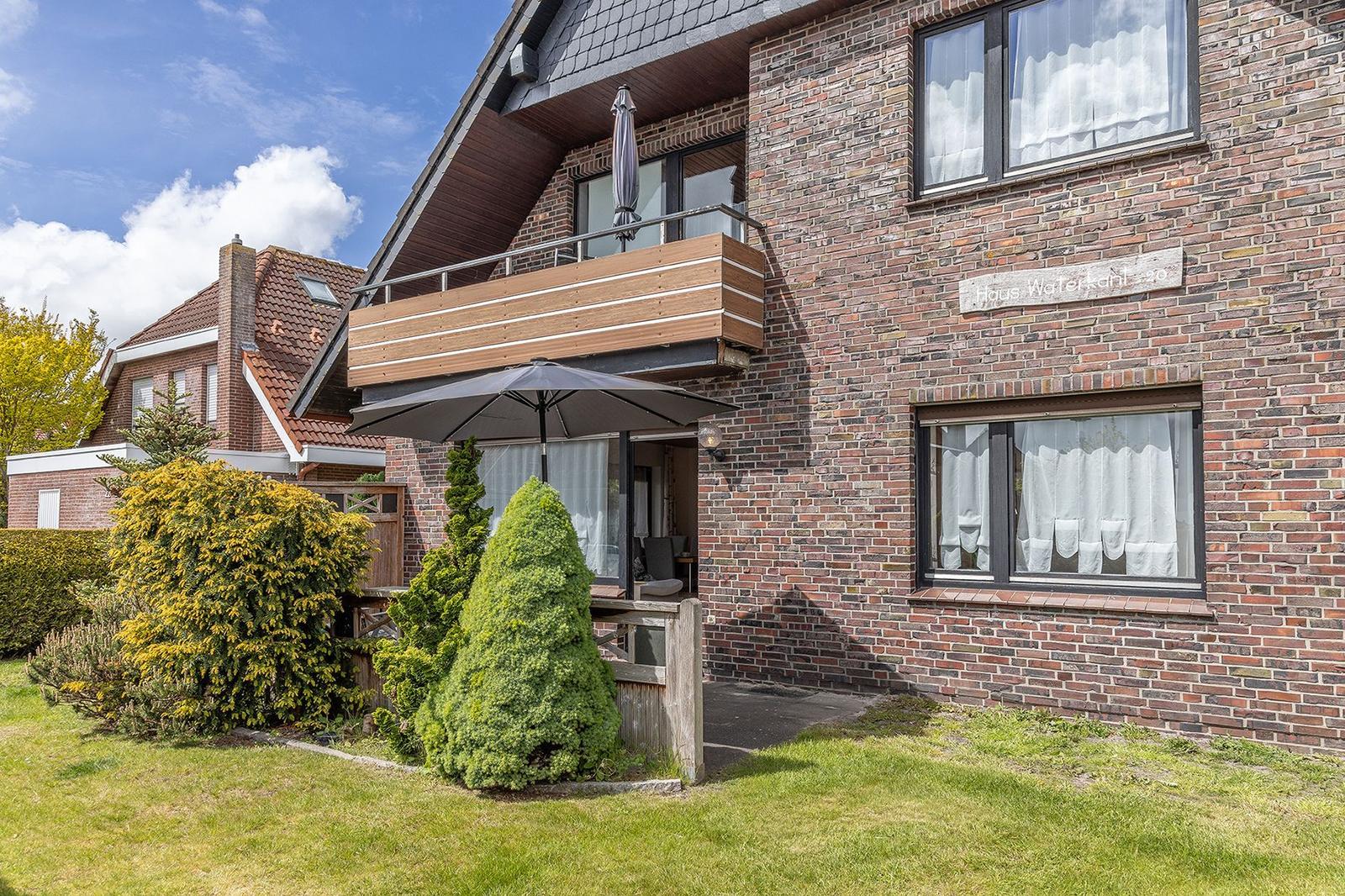 Haus mit Balkon, Terrasse und Garten. Fassade aus Backstein. Fenster mit weißen Vorhängen.