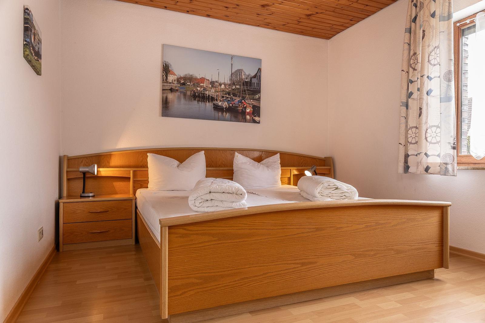 Schlafzimmer mit Holzbett, Nachttisch und Fenster mit Vorhängen.
